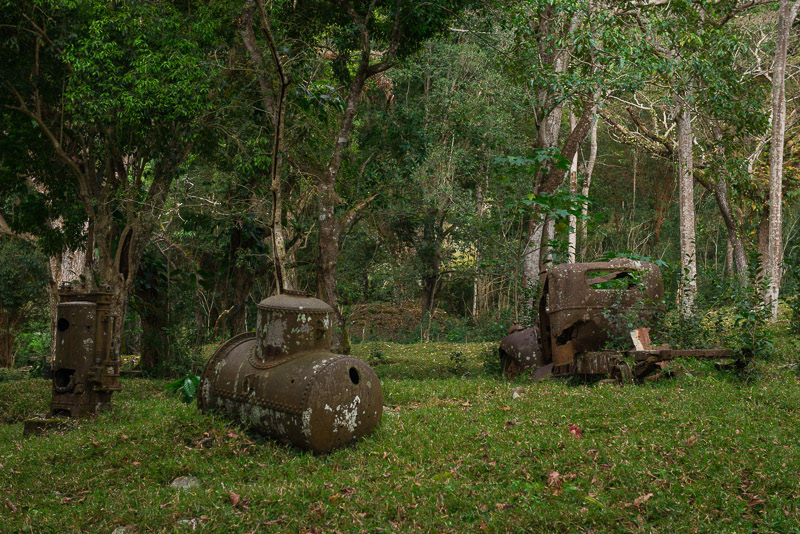 Rusting old boilers and a vintage car in a tropical forest