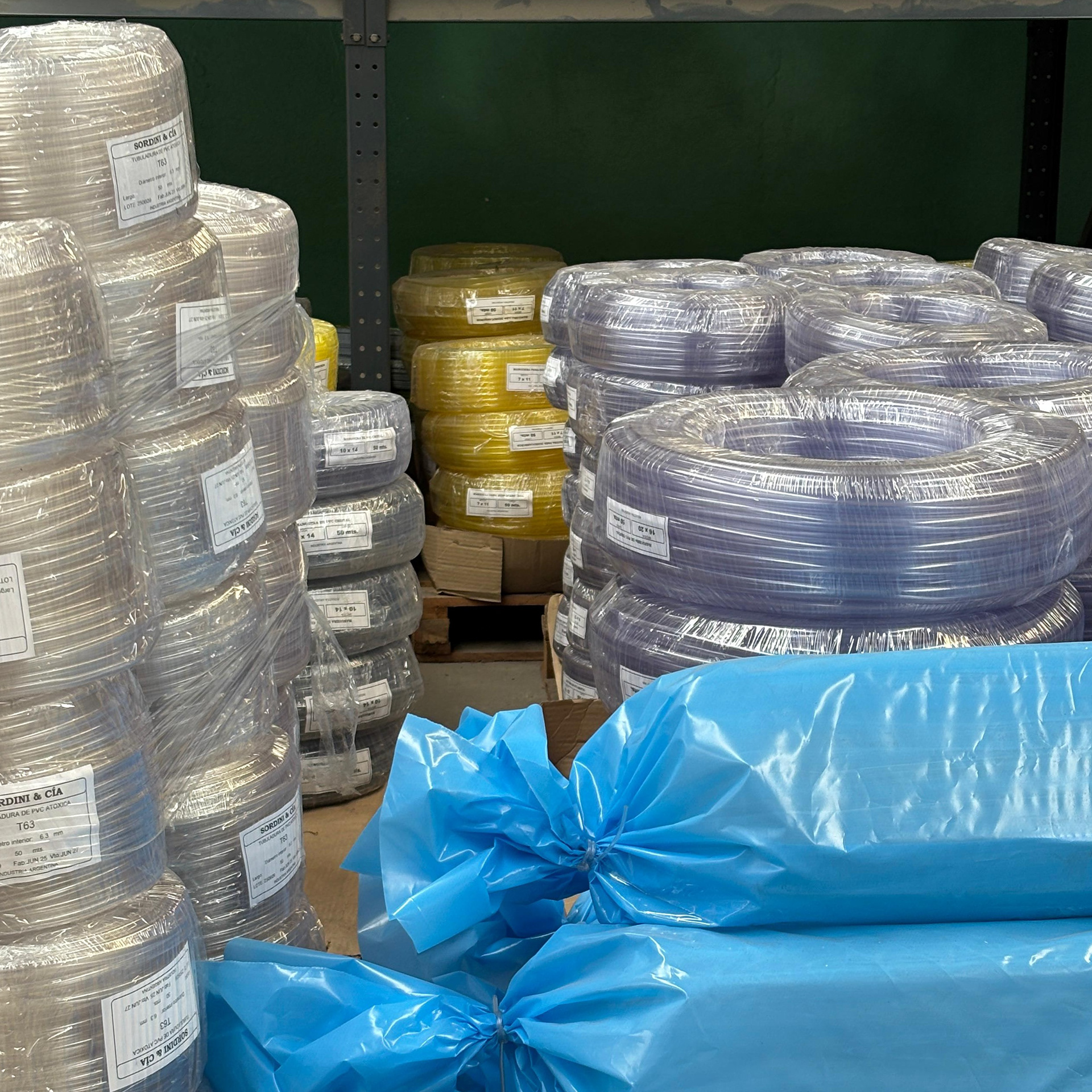 Bobinas de tubos flexibles de PVC virgen en distintos colores, embaladas y apiladas en el sector de depósito. Incluye etiquetas identificatorias y envoltorios plásticos.