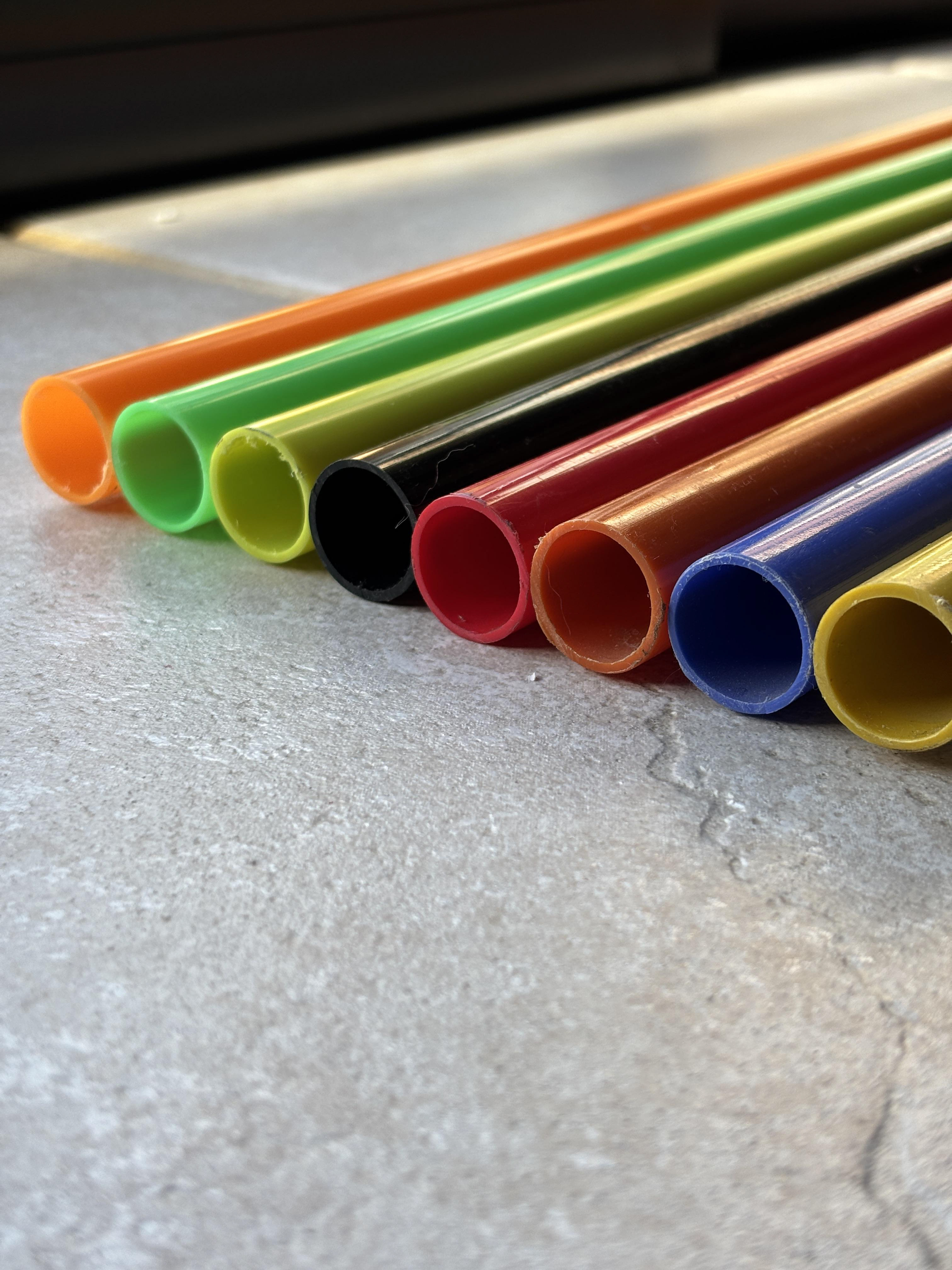 Tubos de PVC rígido en una gama de colores vivos (naranja, verde, amarillo, negro, rojo, azul, entre otros), dispuestos sobre superficie clara.