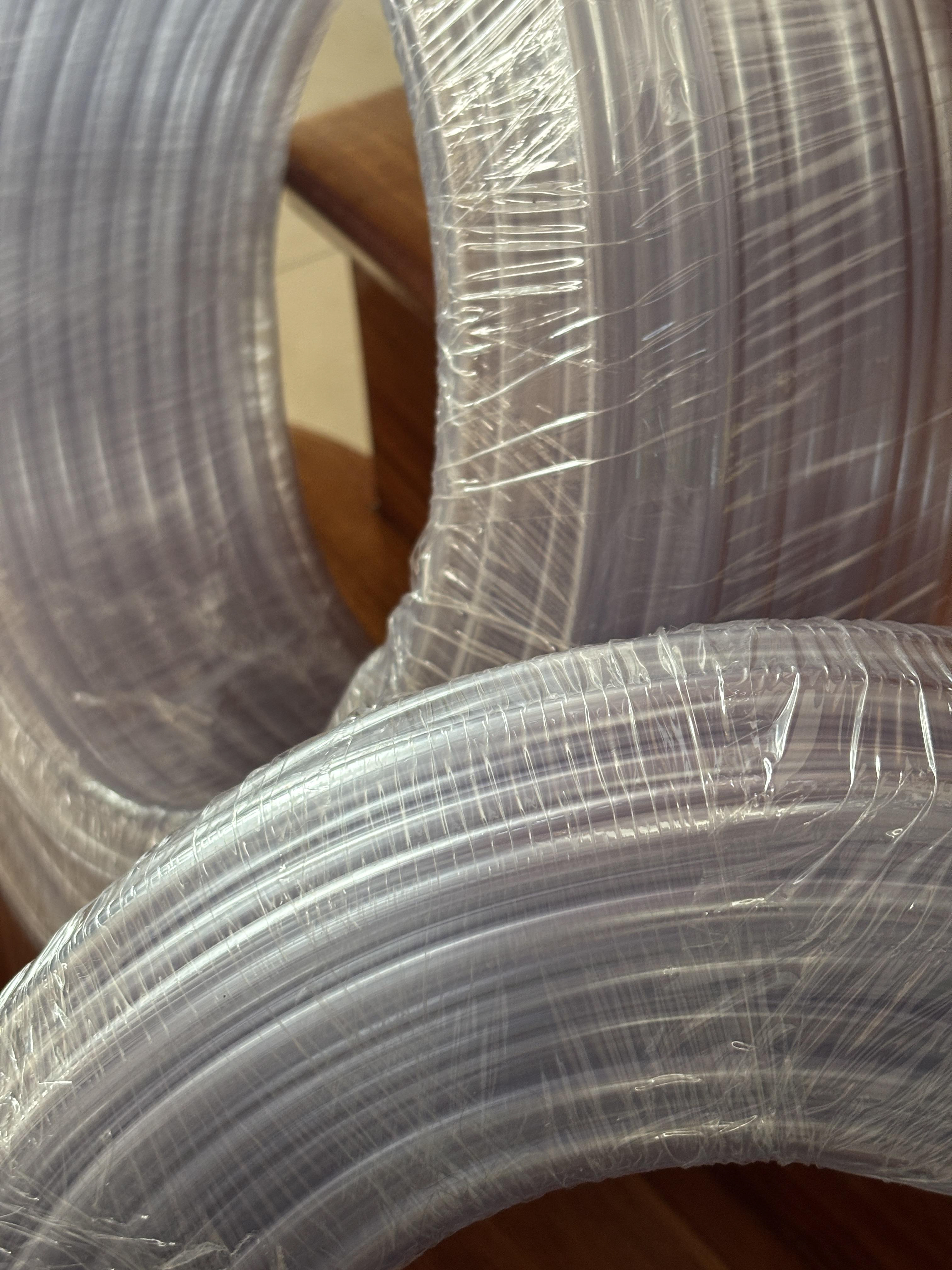 Primer plano de bobinas de tubos flexibles de PVC virgen transparente, envueltos en film plástico para su almacenamiento o distribución.