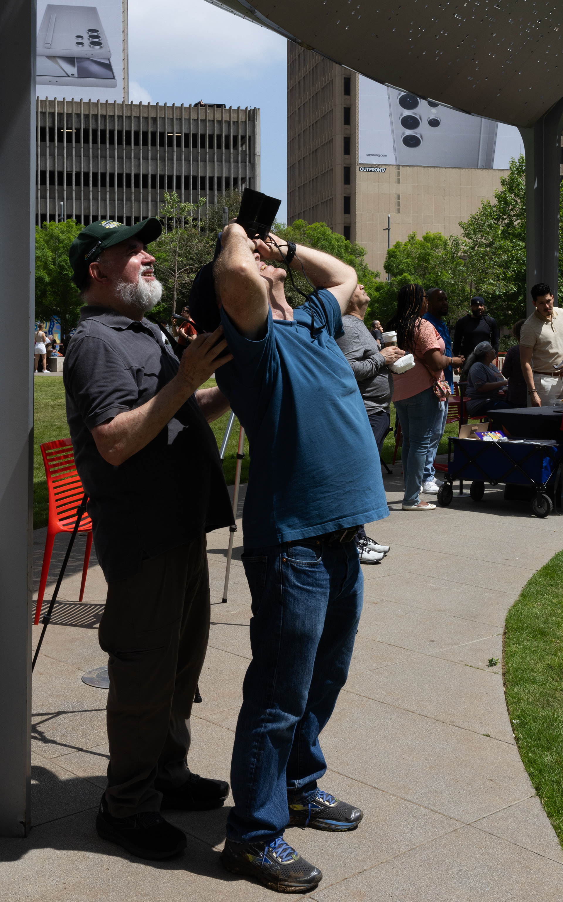 DalTwo men help eachother observe the passing eclipse taking turns using their binoculars.