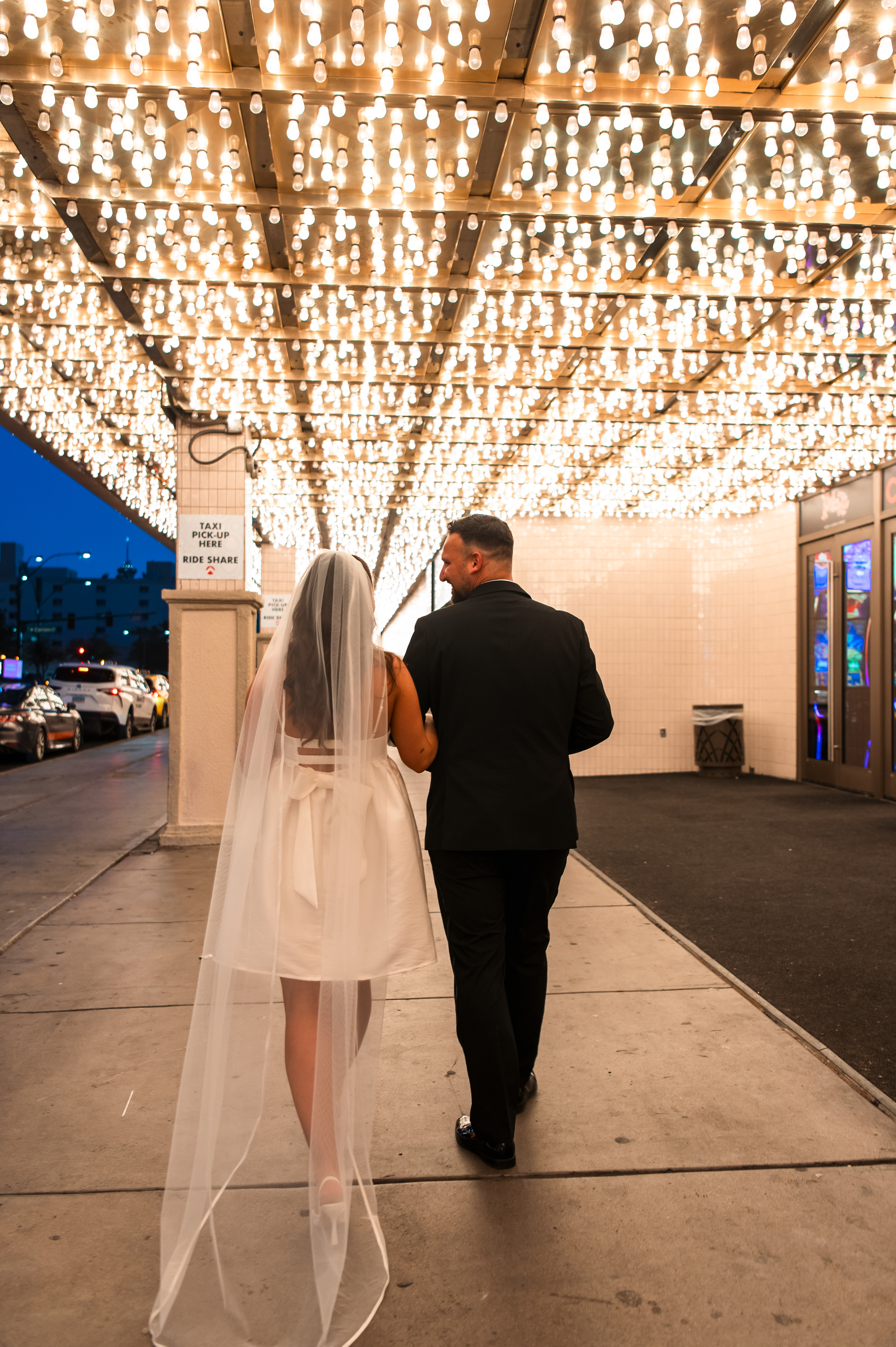 Newlyweds walking beneath the glowing marquee lights of the Plaza Hotel & Casino during a downtown Las Vegas wedding photo session.