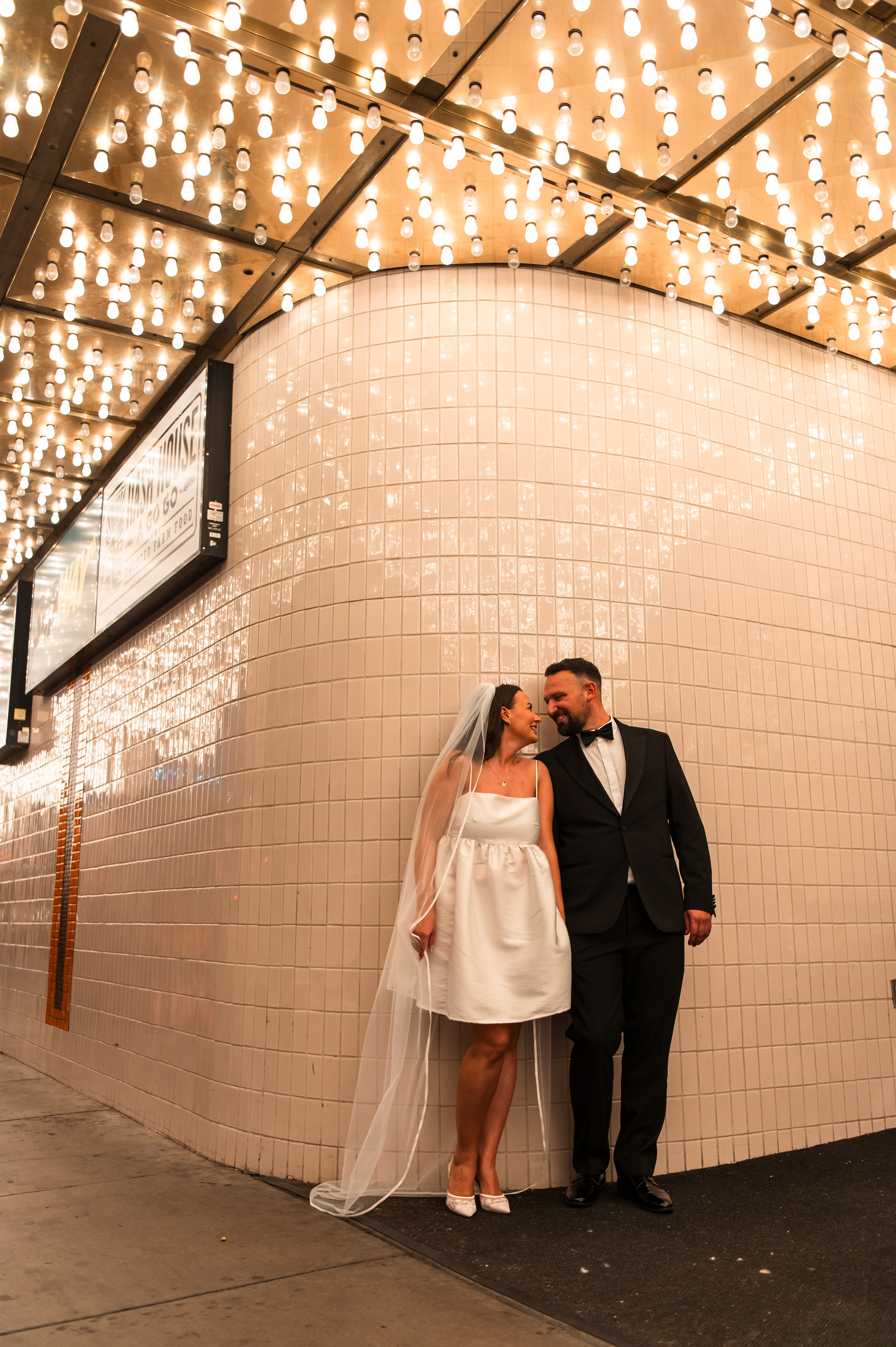 Bride and groom posing beneath the vintage marquee lights along the Plaza Hotel & Casino in downtown Las Vegas.