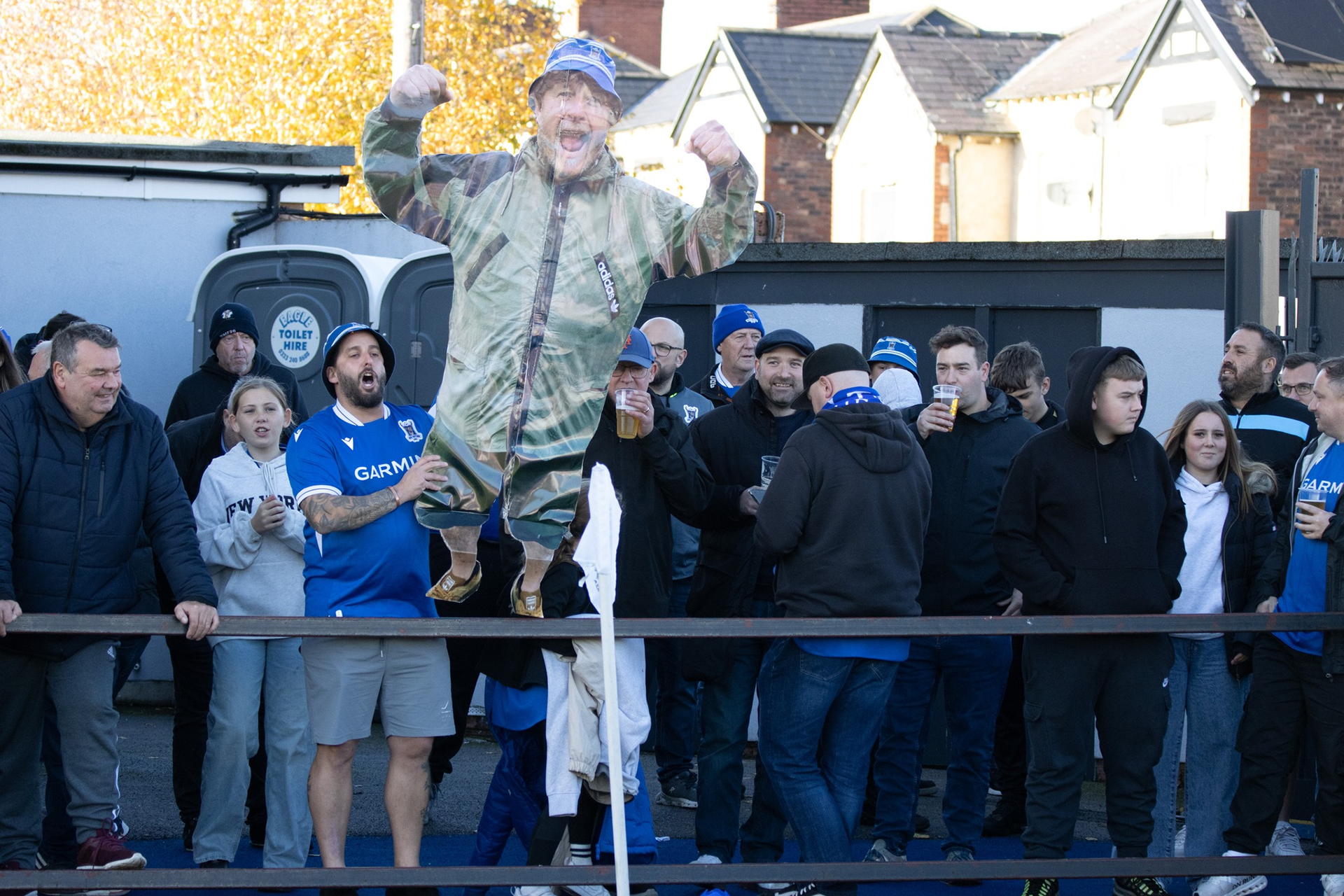 An AFC Totton fan holds a cardboard cut-out of another fan aloft in the away end,