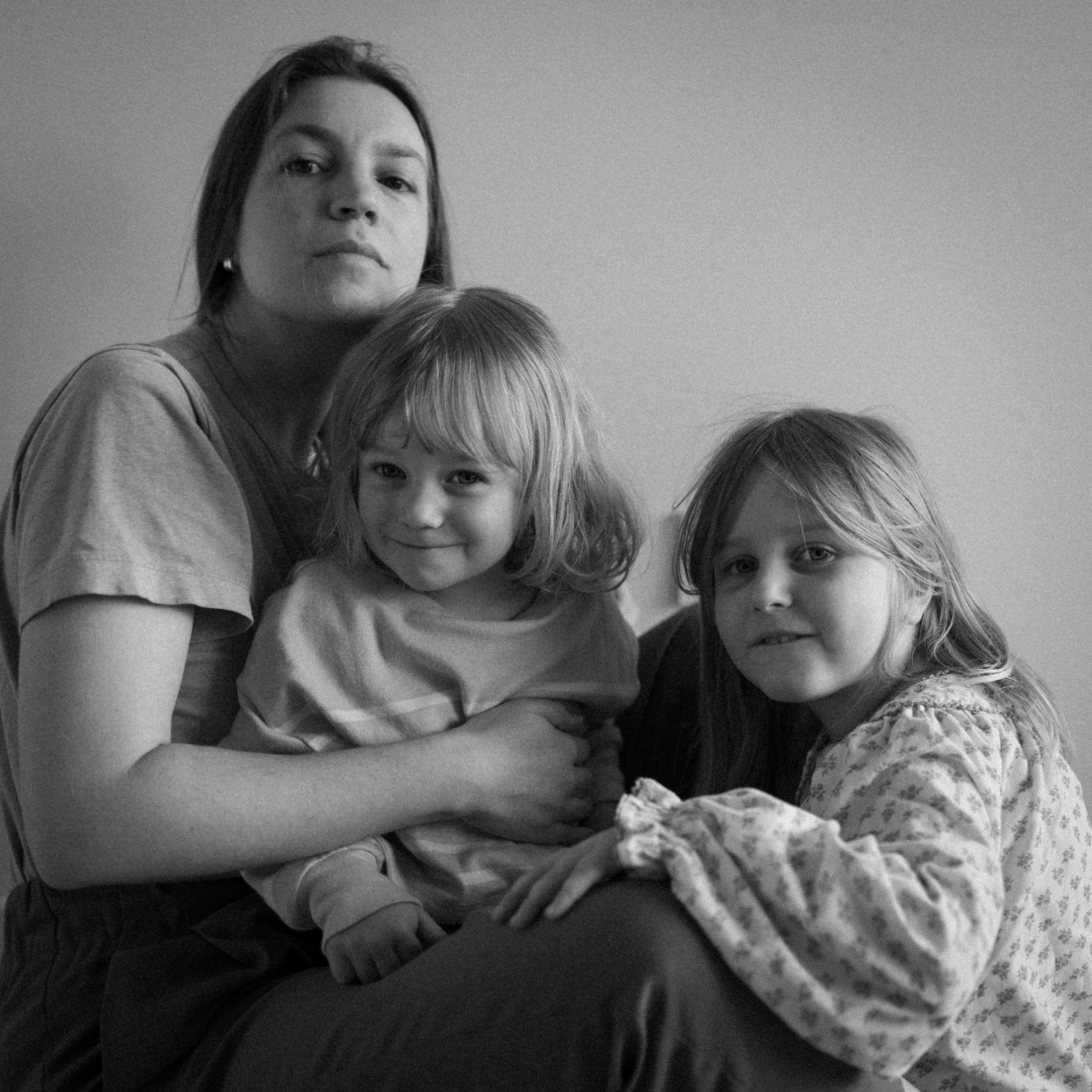 Une maman et ses deux enfants dans les bras sont assis ensemble par terre et regardent vers l'appareil photo