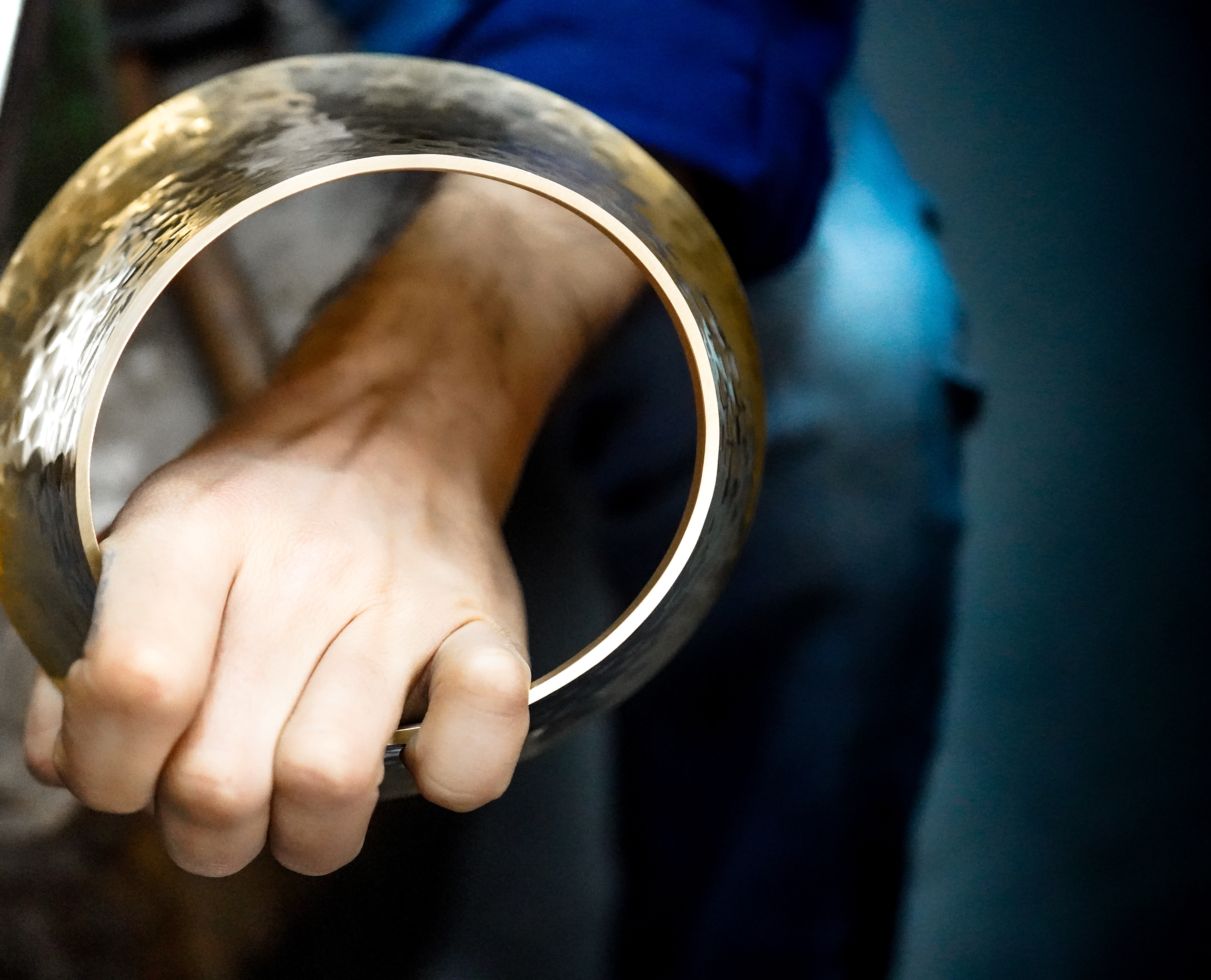 Geste d'artisan d'art travaillant le laiton - Le joaillier KARL MAZLO travaille le métal pour la création de bijoux d'exception. Main tenant un collier de laiton, fabriqué pour la présentation de collection de LOUBOUTIN. Photographie savoir-faire et artisanat d'exception par Béatrice Prestage