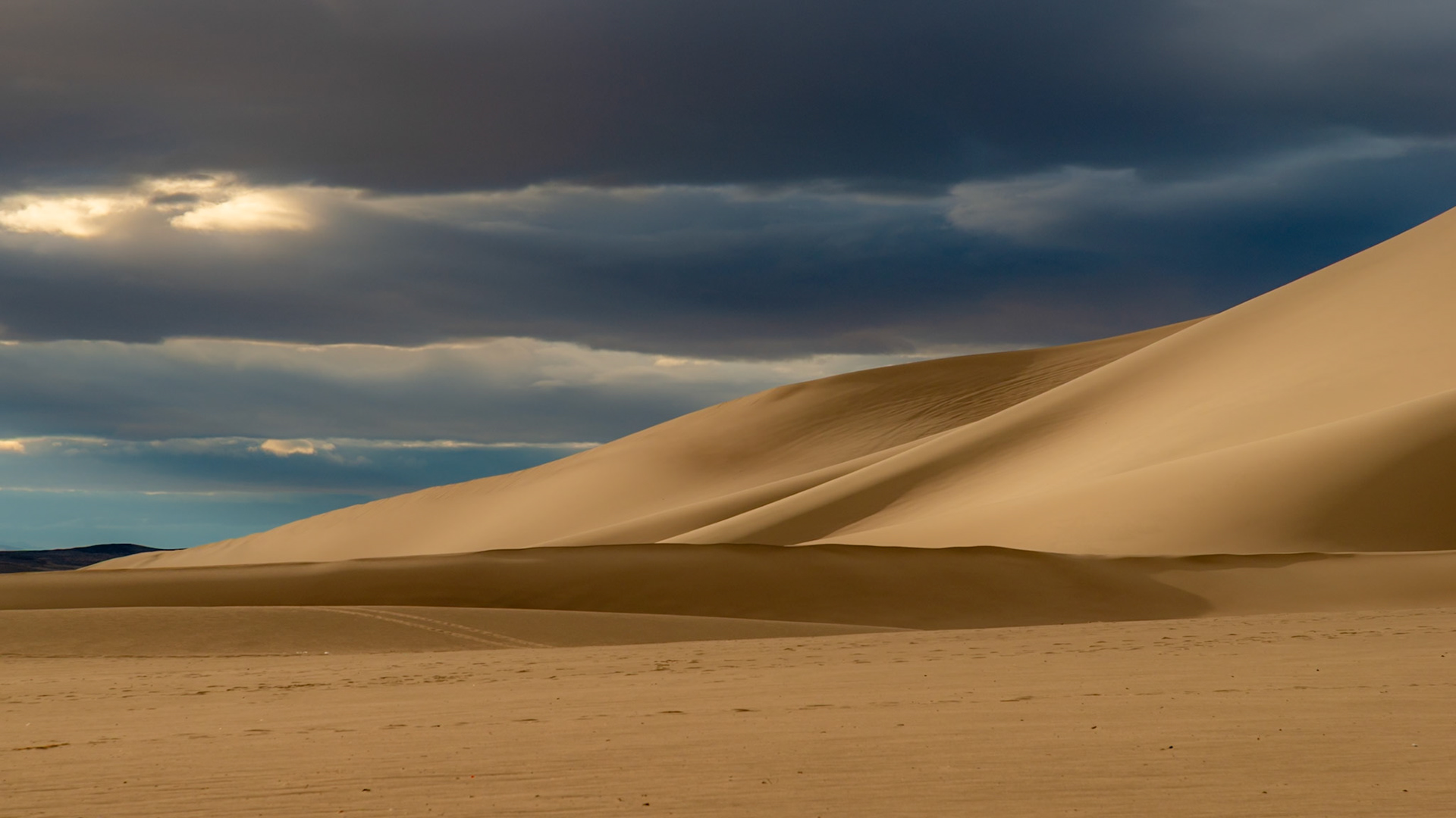 Dramatic clouds and sun cast light and shadows on the dunes at Sand Mountain Recreation Area in Nevada.
