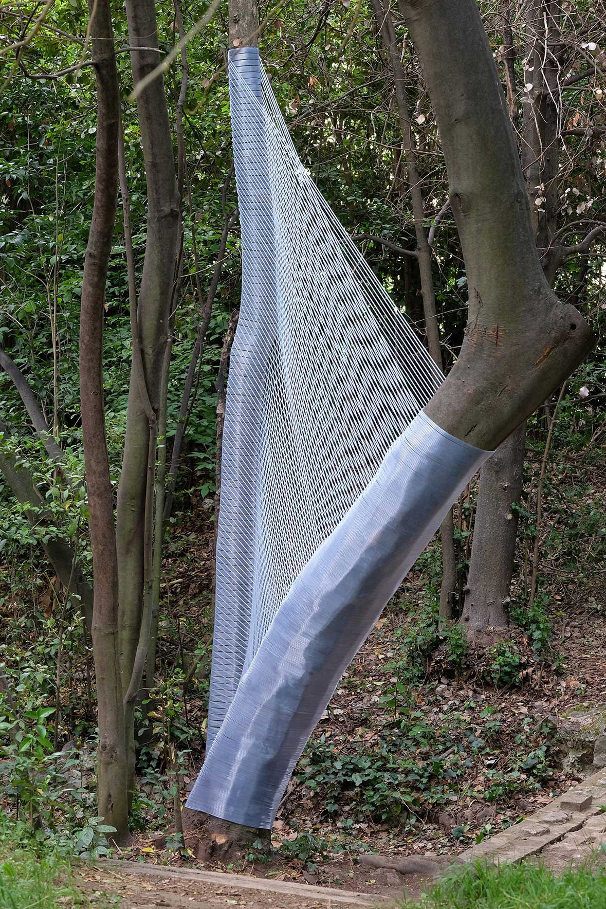 arbres éthérés - fil pvc translucide de Ø 5 mm - environ 450 x 350 x 150 cm. Œuvres in situ réalisée pour “Occurrence” la 14e édition des Arts Éphémères - Parc de maison Blanche Marseille - mai/juin 2022 - © photos Arnaud Duboistesselin. Deux arbres aux troncs disparates sont réunis dans une sorte de symbiose visuelle. Une intimité qui fonde la forme de l’œuvre. Le fil pvc translucide permet à la structure de changer d’aspect selon la lumière du moment et la situation du regardeur. Ainsi, à l’instar d’une toile d’araignée s’invitant dans son milieu naturel, ce grand maillage installé à l’orée d’un sous bois, bien qu’il s’intègre facilement dans le paysage, appelle, grâce à son étrangeté plastique, à de multiples évocations poétiques comme ésotériques. N.B. le fil pvc est récupéré pour une autre possible installation.