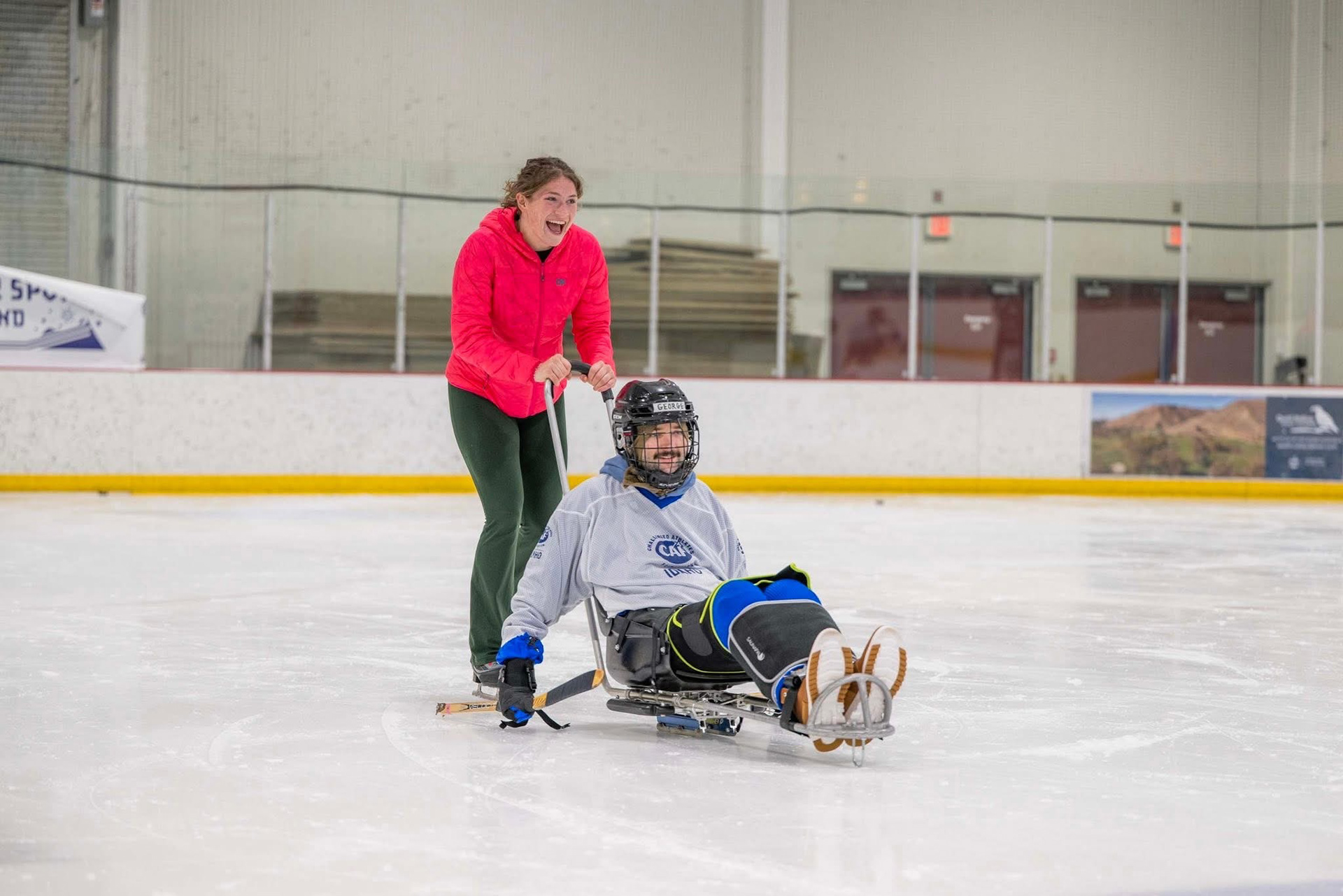 George skating in an ice sled, being pushed by his girlfriend, Halle. 