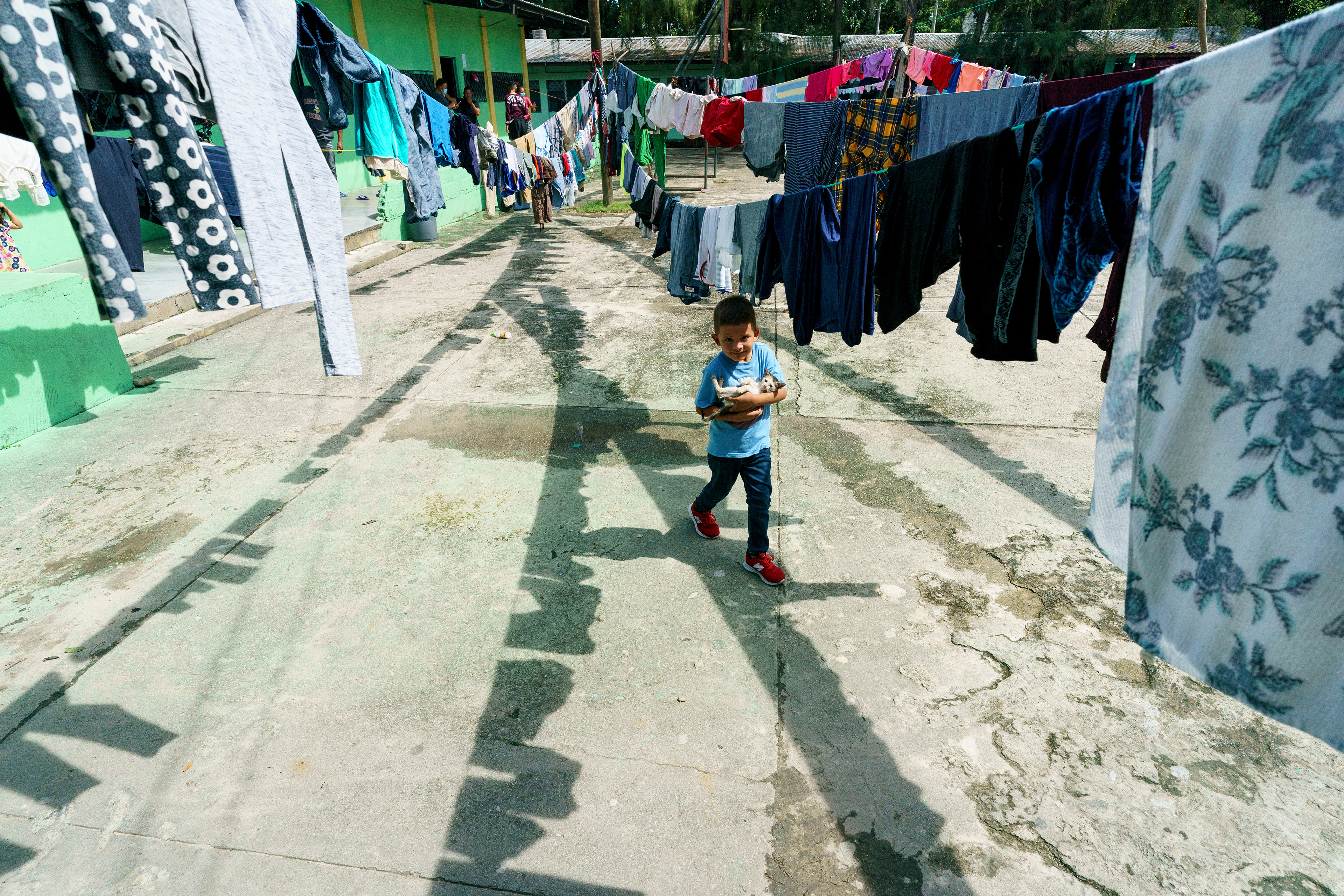 A boy holds a kitten as he walks among drying wash in a school converted to a family shelter to house those displaced by Hurricanes Eta and Iota in Choloma, Honduras.