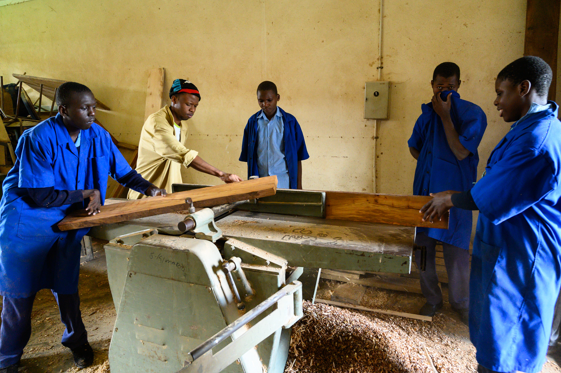 Carpentry instructor Emanuel planes boards with Training Class students. The classes ready students with learning and physical disabilities to enter Tanzanian society.