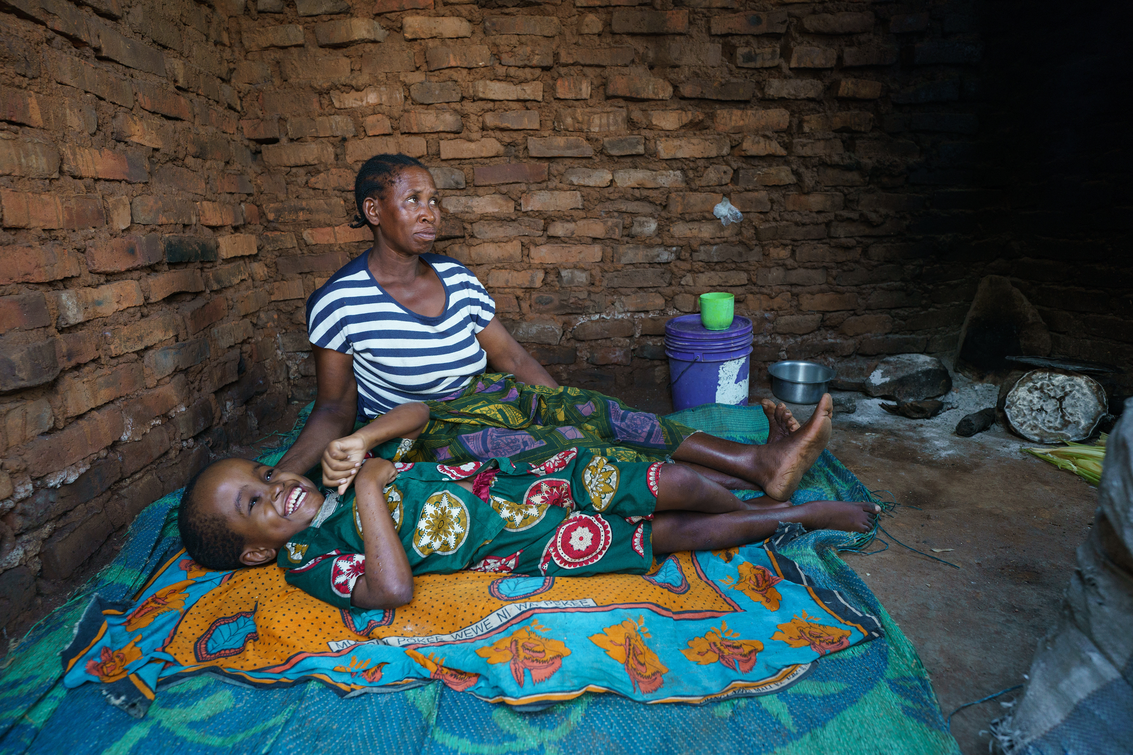 Abraham Angelos, 12, lies in the family's cooking shelter with his mother Katherine Anthony near the village of Romero, Tanzania. He has untreated hydrocephalus resulting in developmental delays and neuromuscular problems. Still, he laughs easily, is partially verbal, and loves to sing. 
