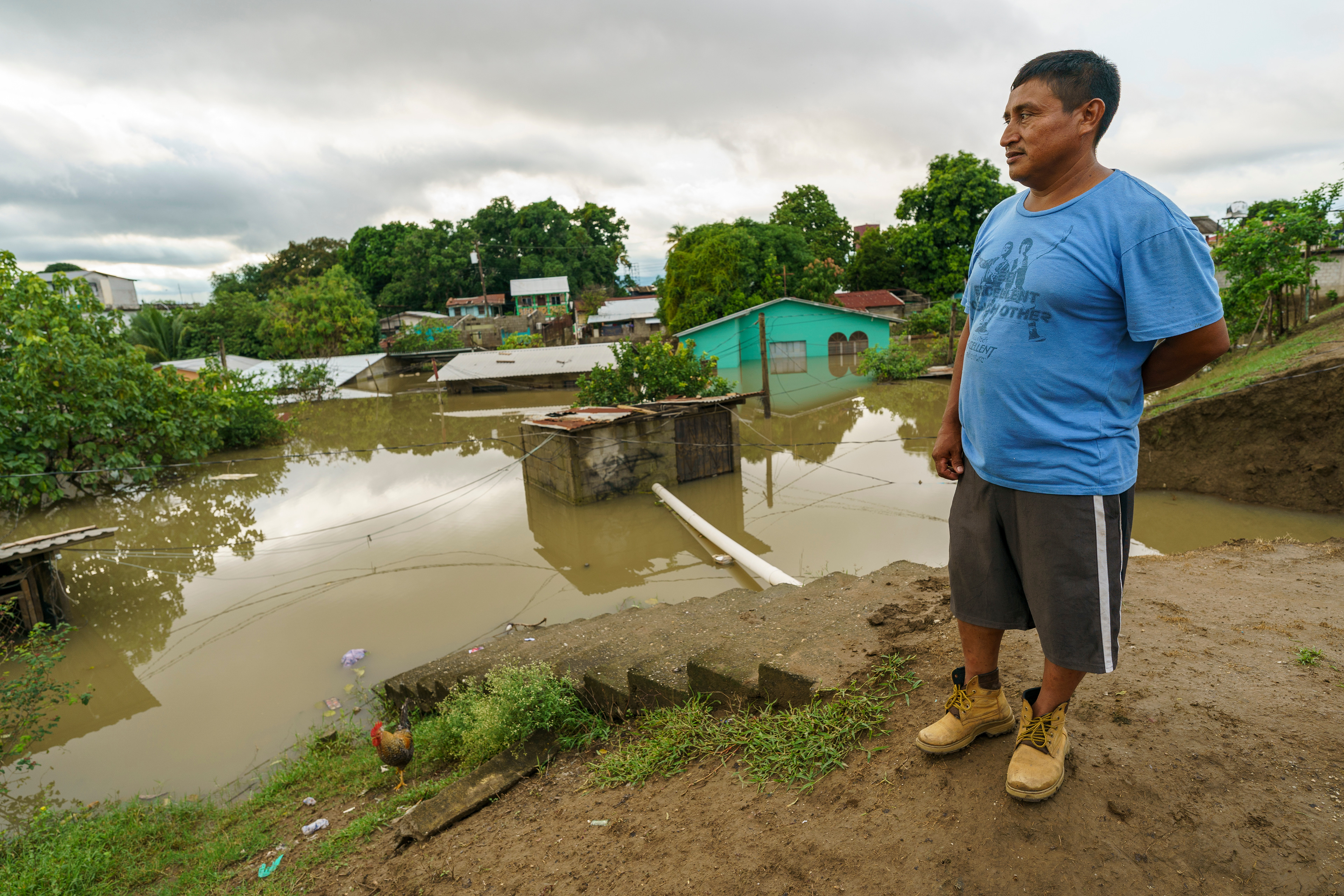 Elio Gomez stands on the breached levee (background) in La Lima, Honduras, assessing the flooded town following Hurricane Iota.