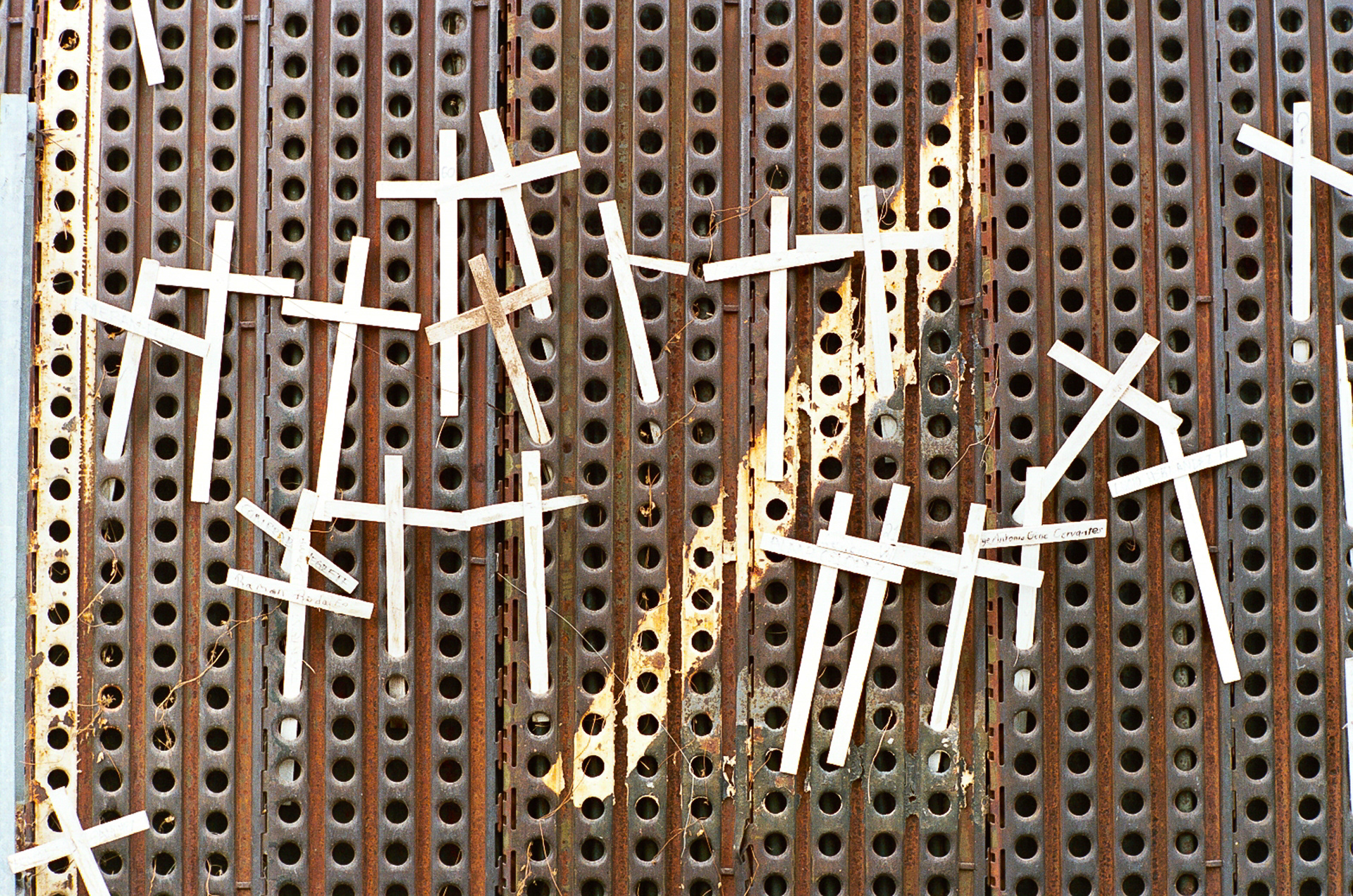 Crosses marking a death of a loved one hang on the border fence in downtown Nogales, Mexico. On each cross is written the name of the deceased and how they died. Many die from dehydration, others from robbery or molestation. Some causes are unknown. An interesting point of trivia is that the holed panels these crosses hang on are recycled landing strip plates sent back from Kuwait and Iraq after the first Gulf War. They were used to build temporary airports on the desert sand.