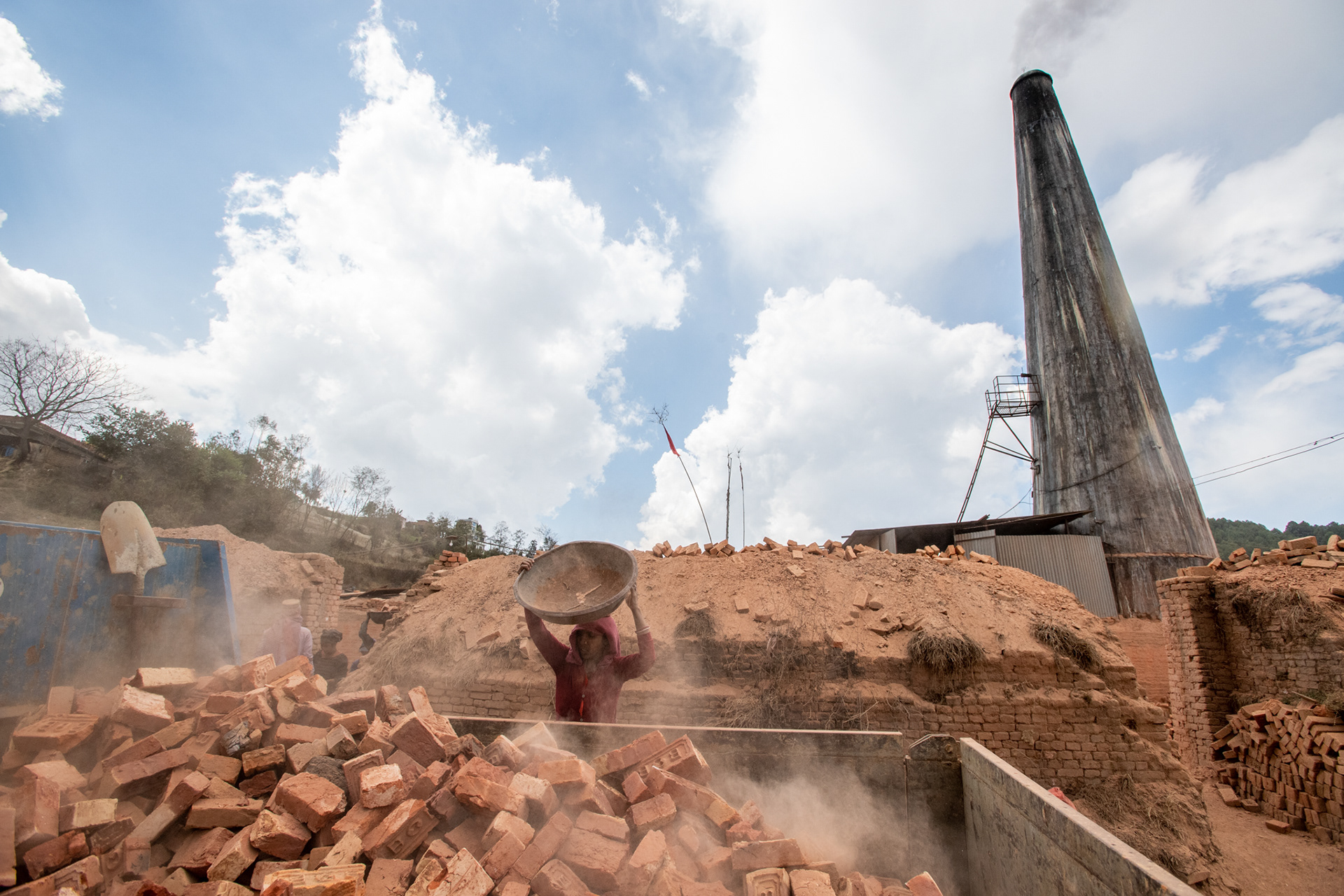 The kiln's smokestack looms large over the workers as they load a truck with discarded bricks.