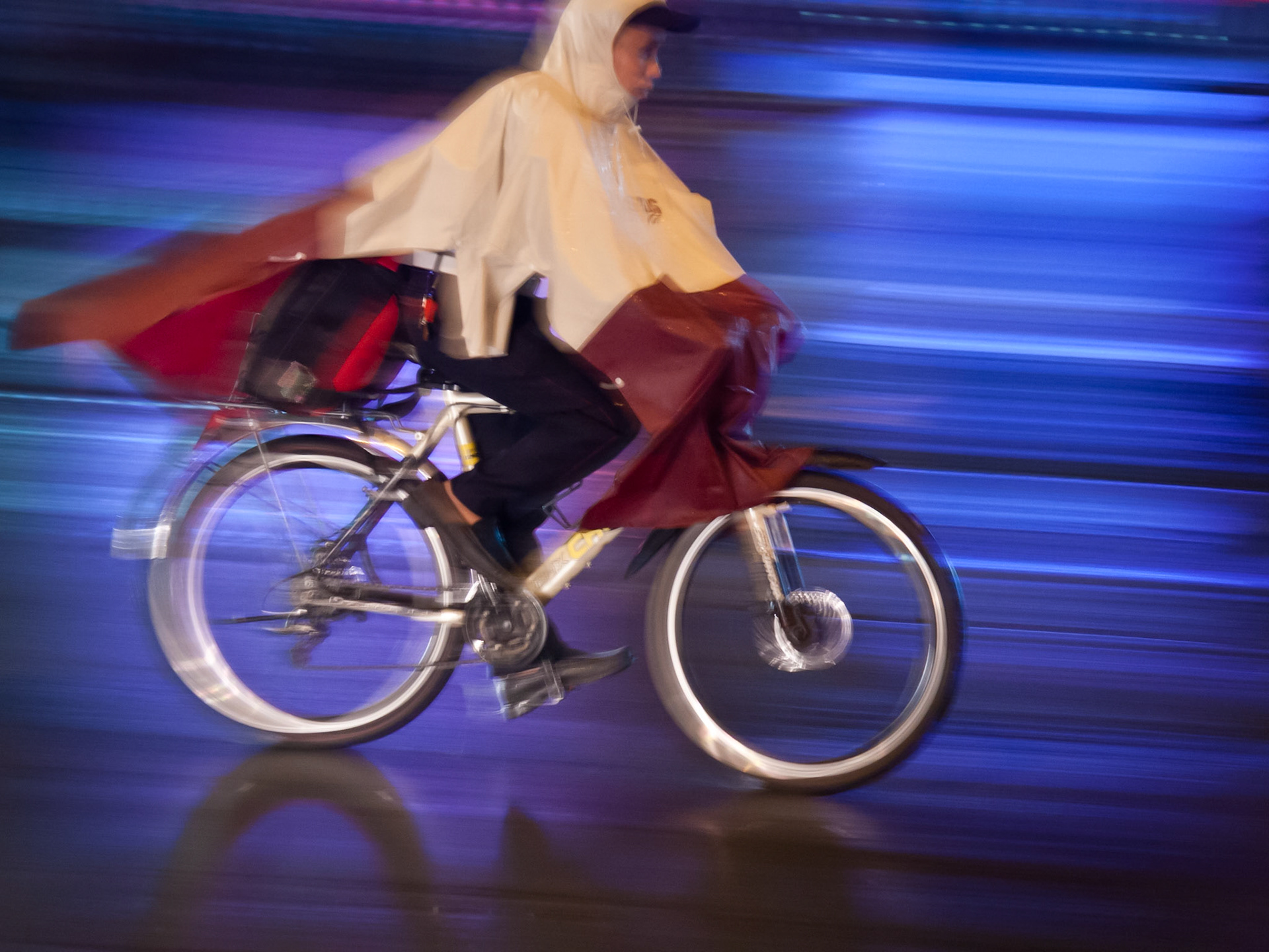 Slow pan of a cyclist lit in the headlights of cars at the traffic light.