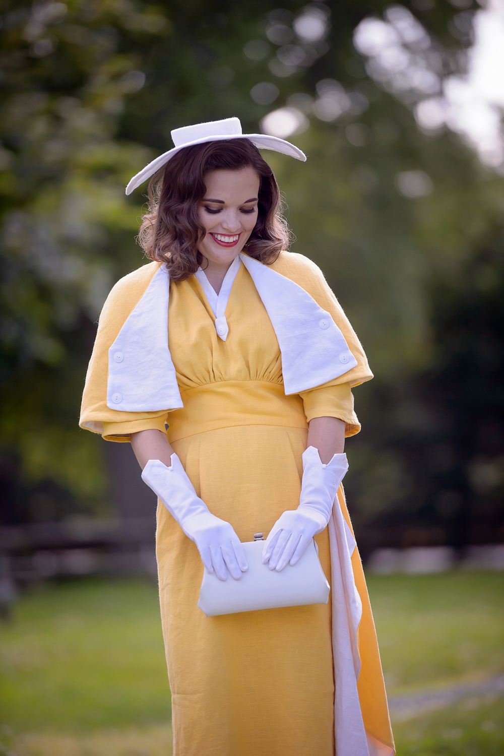 Late 50s Day Dress & Capelet: This yellow linen dress has a pencil skirt pleated at the waist and raglan sleeves, all capturing the iconic 1950s silhouette. The look is completed with a matching capelet and decorative waterfall detail in the skirt, color-blocked with white linen.