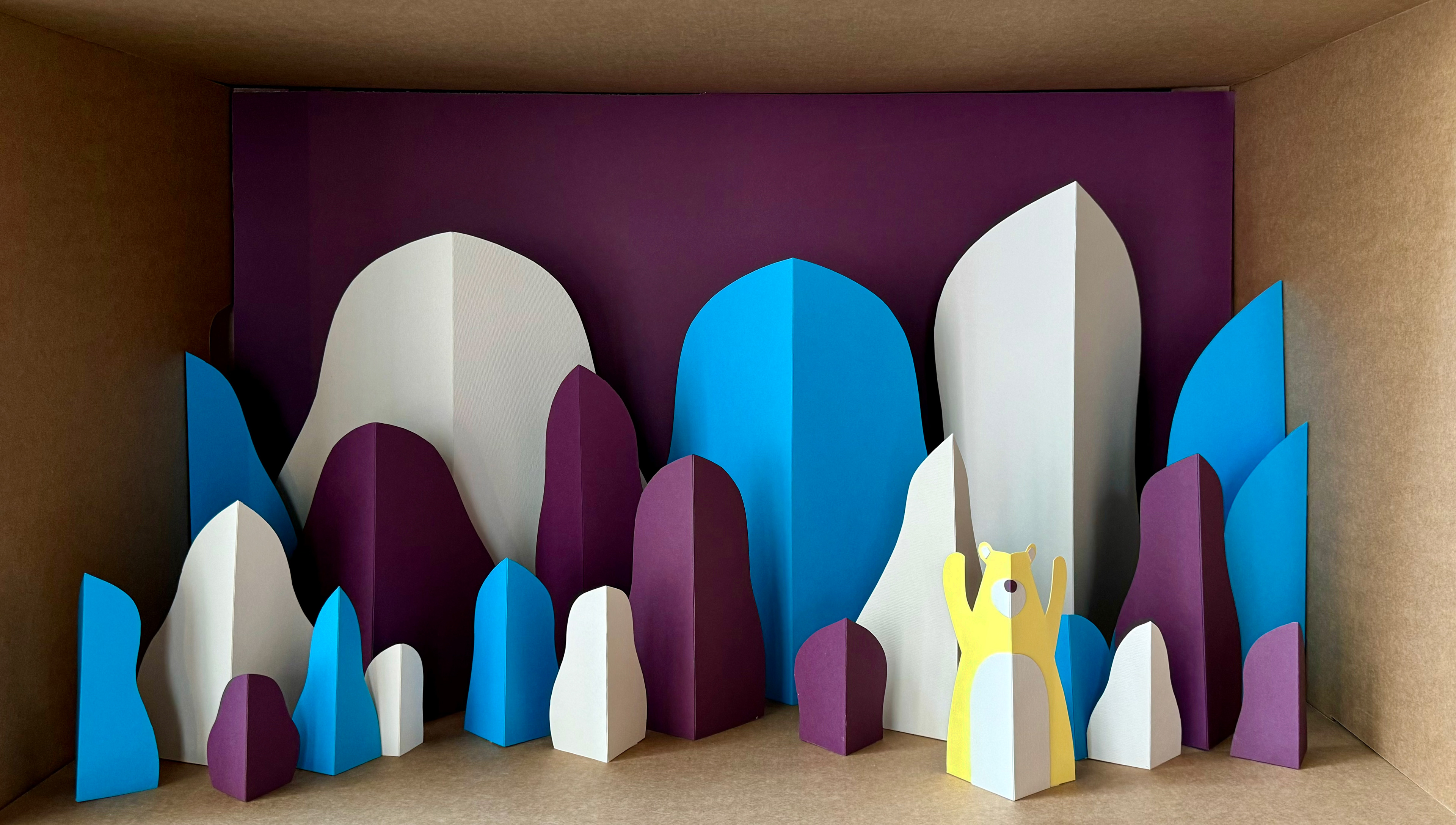 Paper cut installation by Helga Aversa in Illustri Hub, creating a forest scene with bear using colored cardboard, purple, yellow, and blue