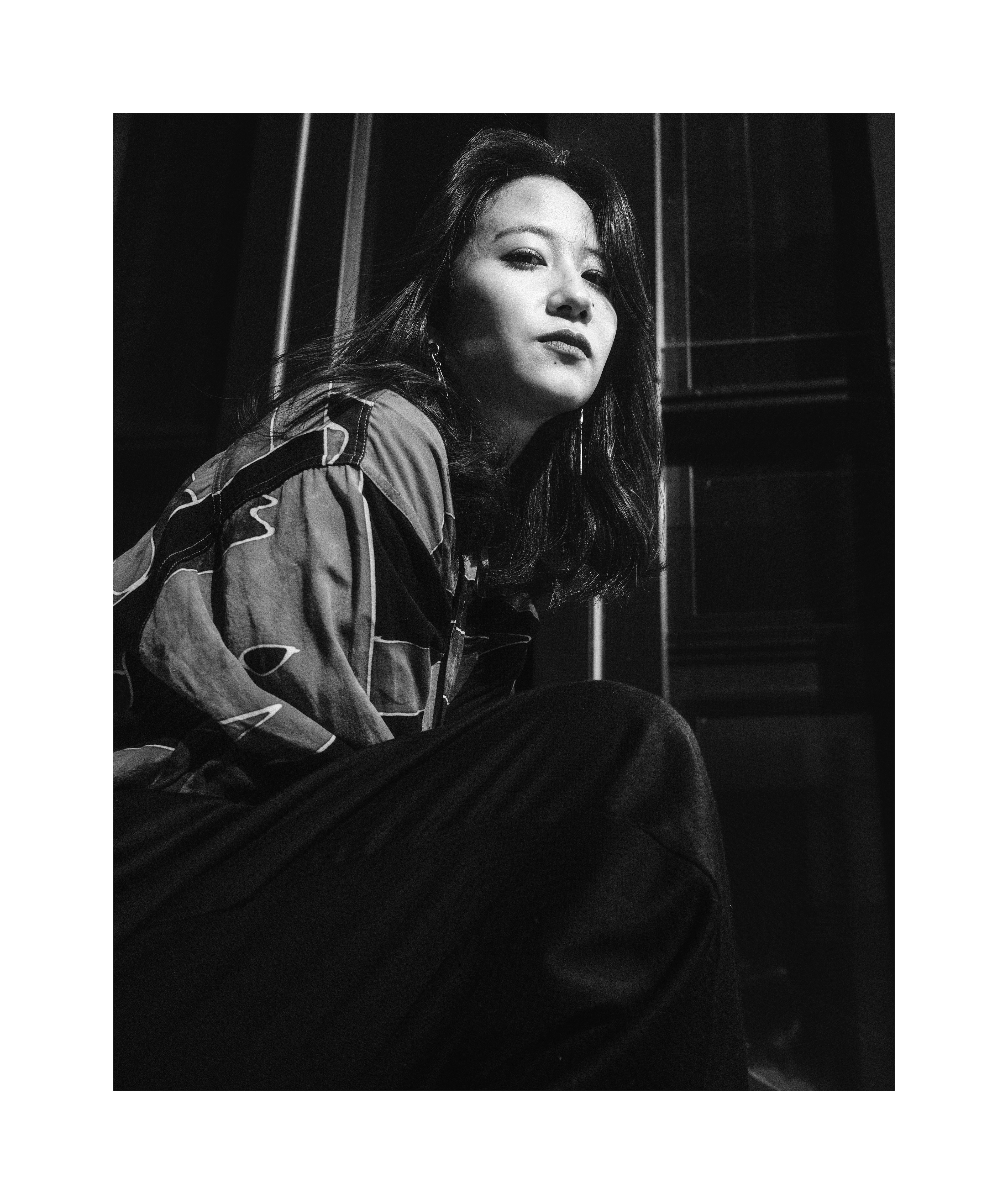 Black and white street editorial portrait of Madoka sitting in dramatic sunlight