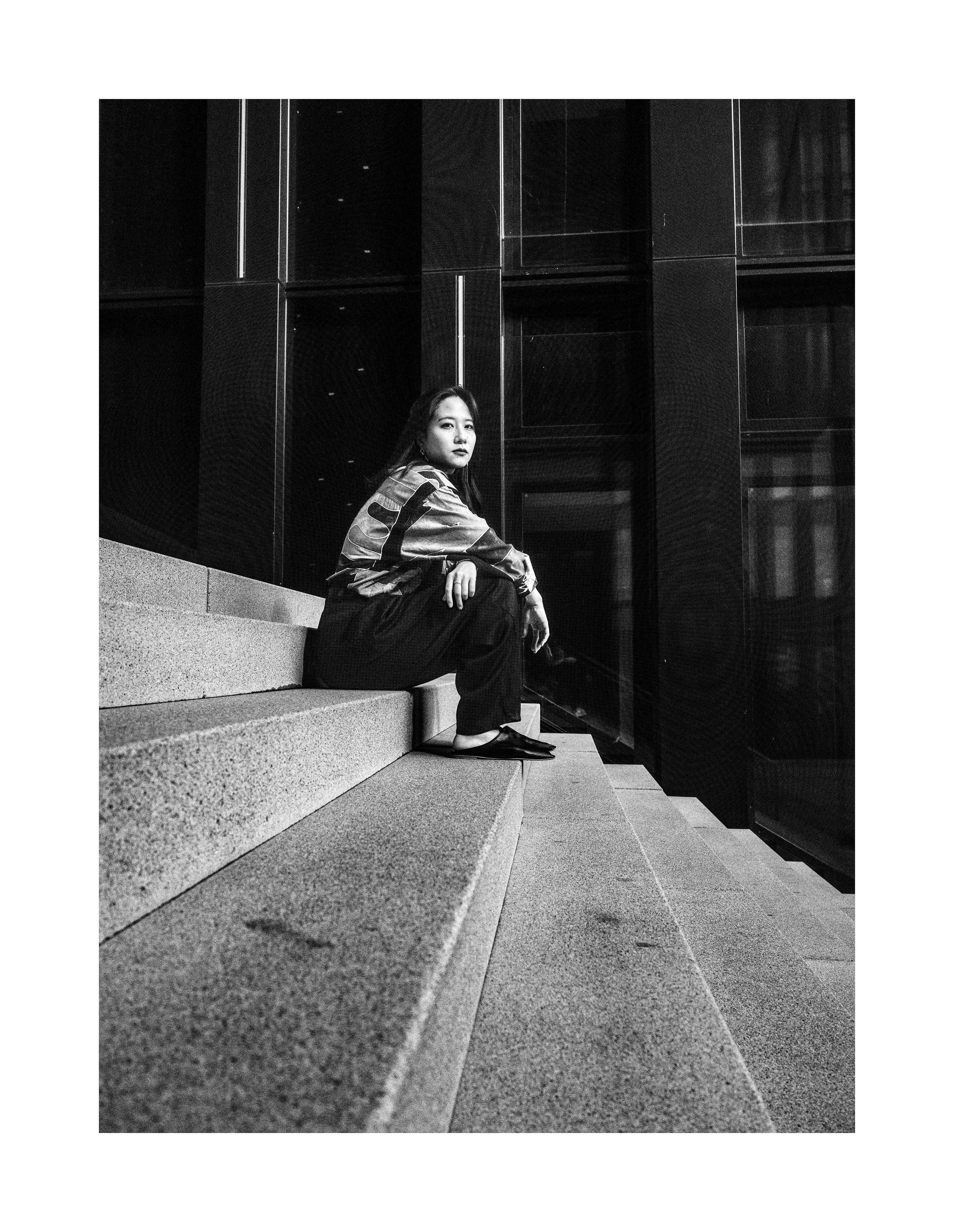 Black and white editorial portrait of Madoka sitting on concrete steps in modern urban architecture