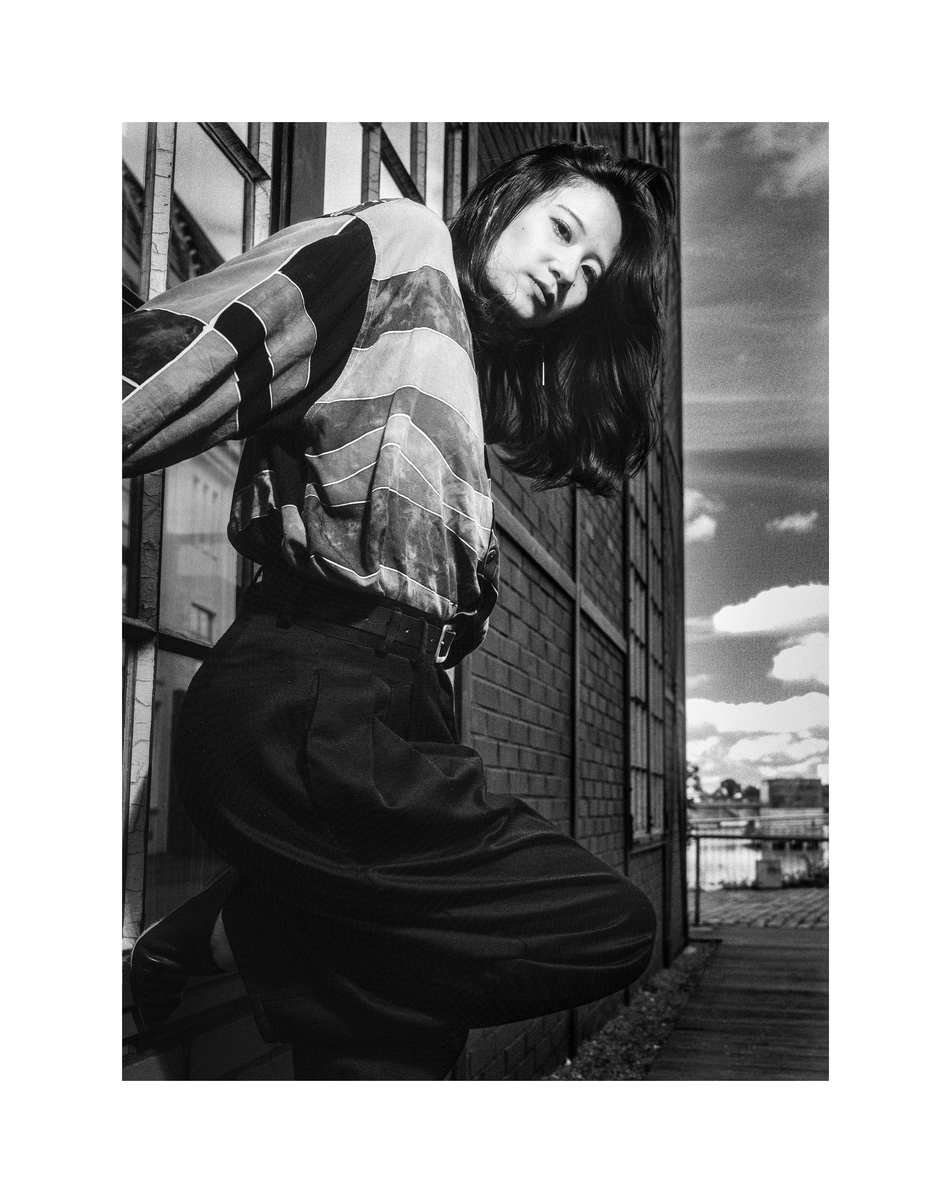 Black and white street editorial portrait of Madoka posing against an industrial brick wall
