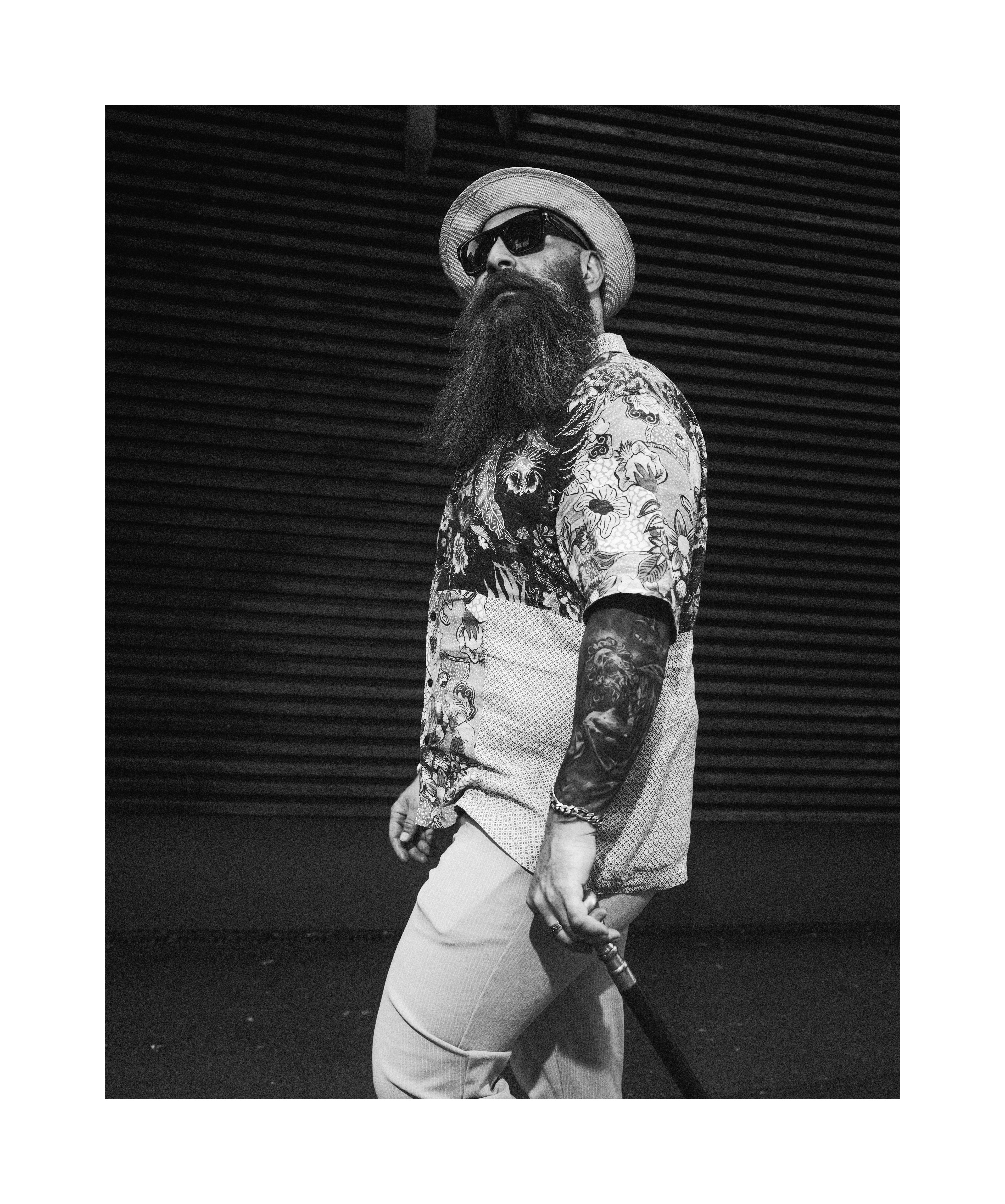 Black and white editorial portrait of a bearded man wearing a hat and sunglasses
