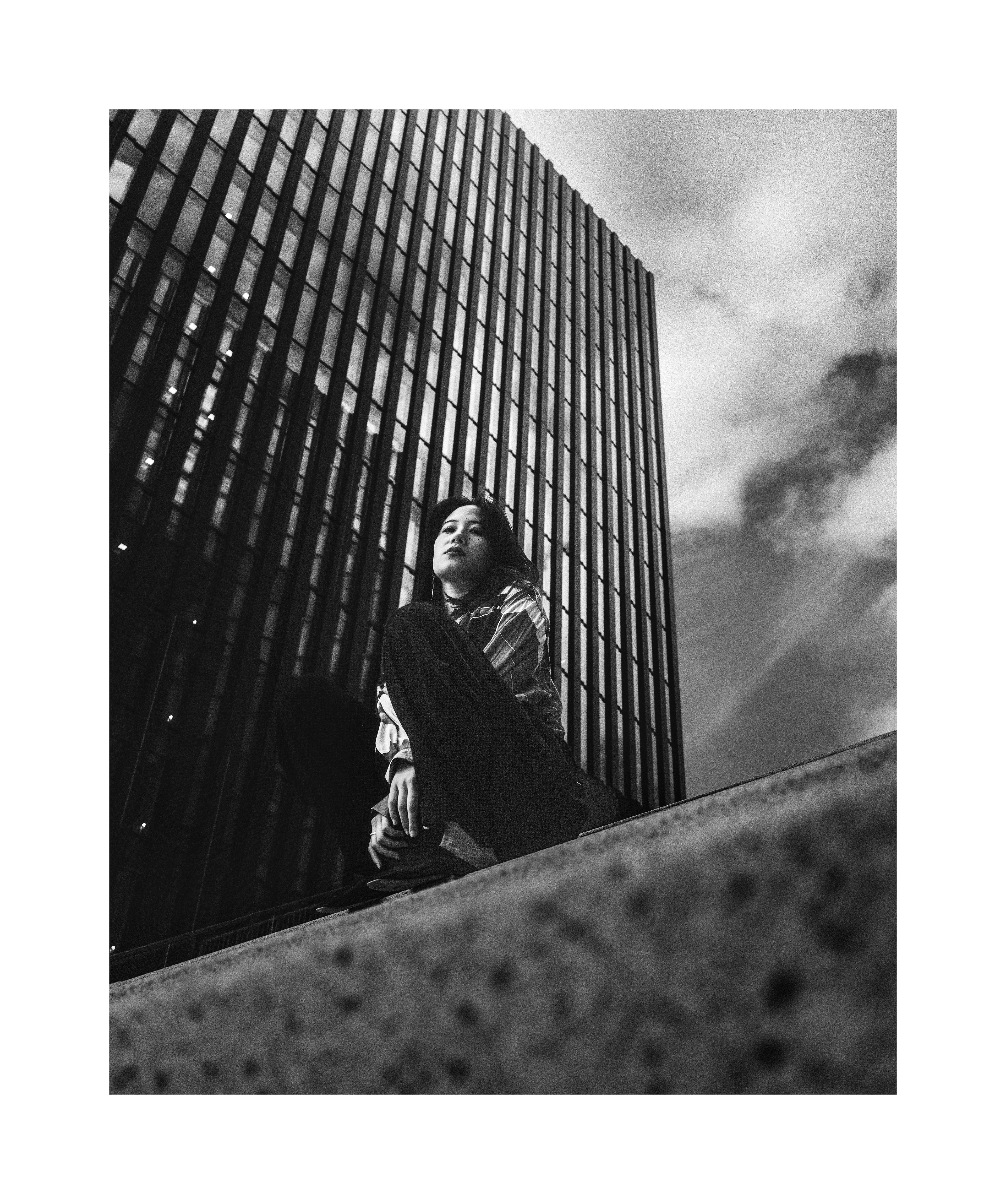 Black and white editorial portrait of Madoka against modern urban architecture