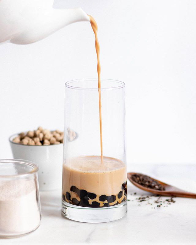 Black milk tea being poured in a clear glass with boba