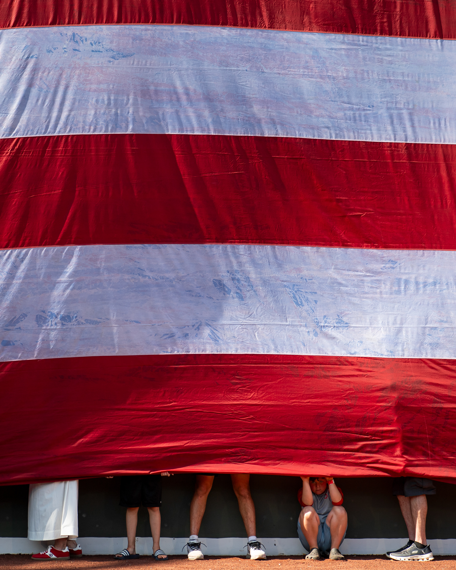 July 25, 2026, Boston, MA: A young fan peeks out from under the American Flag as it is draped over the Green Monster during pre-game ceremonies prior to a game between the Toronto Blue Jays and the Boston Red Sox at Fenway Park in Boston, Massachusetts Saturday, July 25, 2026. (Photo by Aiden Shertzer/Boston Red Sox)