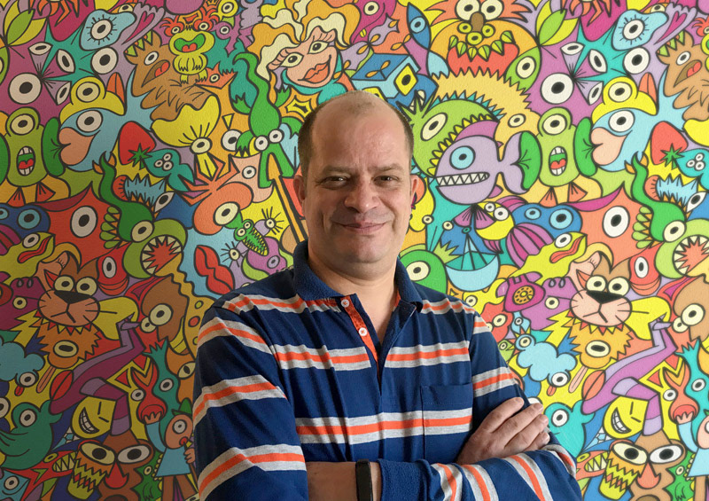 Ronald Reichmann posing against one of his pattern designs printed as a wallpaper