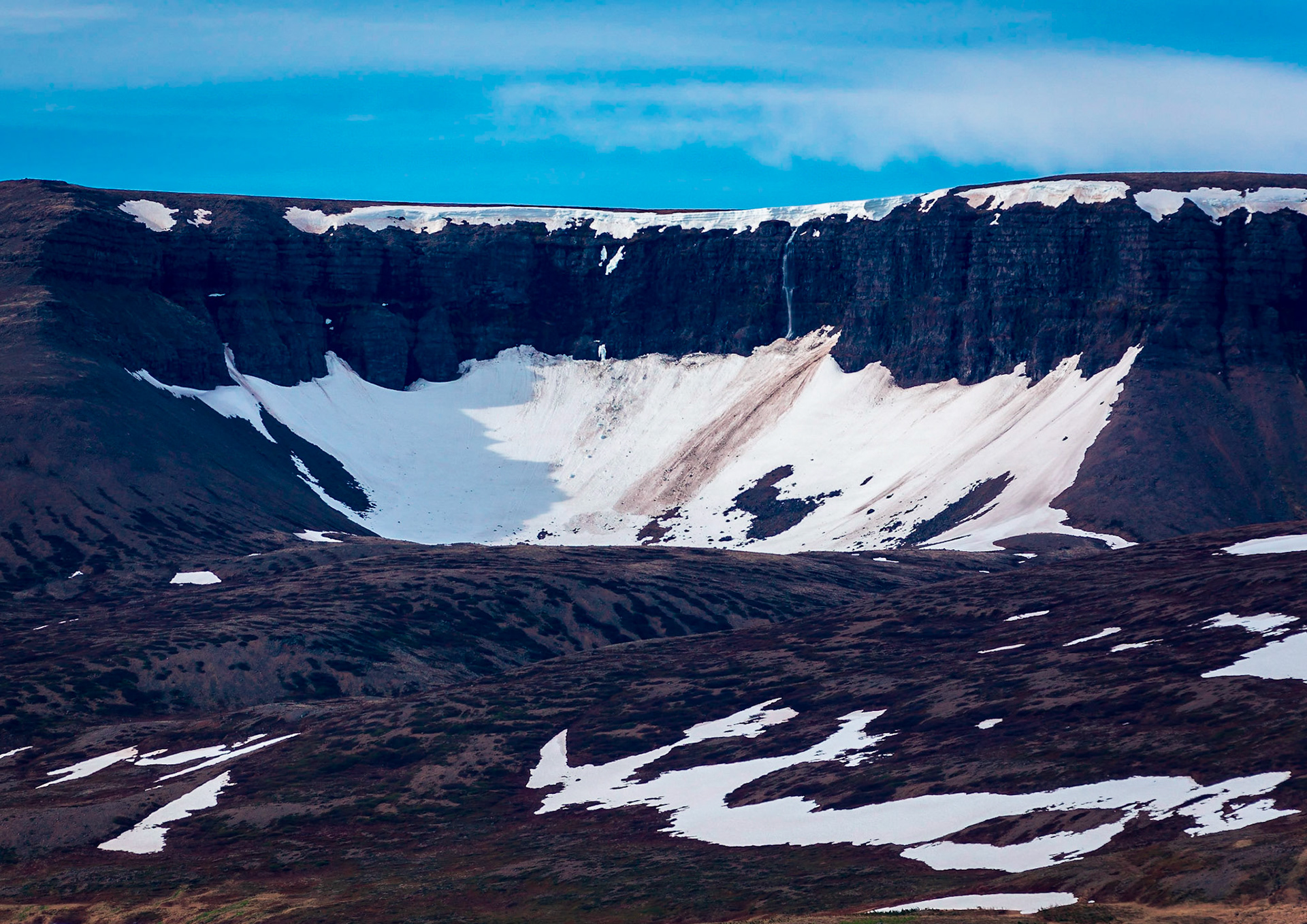 The last snow from winter clings to ca cliff near the small village of Thingeyri or Þingeyri in Iceland in the Westfjords region of Iceland.
