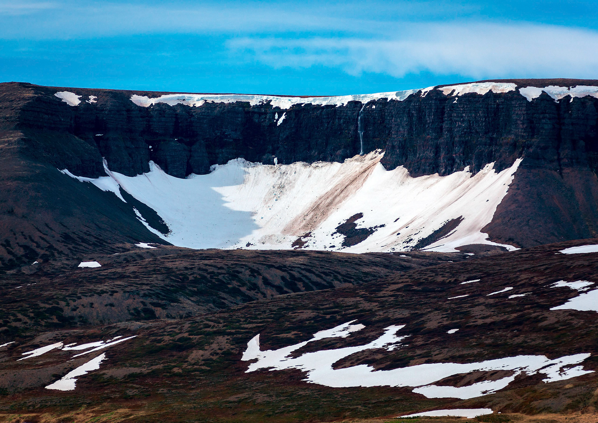 The last snow from winter clings to ca cliff near the small village of Thingeyri or Þingeyri in Iceland in the Westfjords region of Iceland.