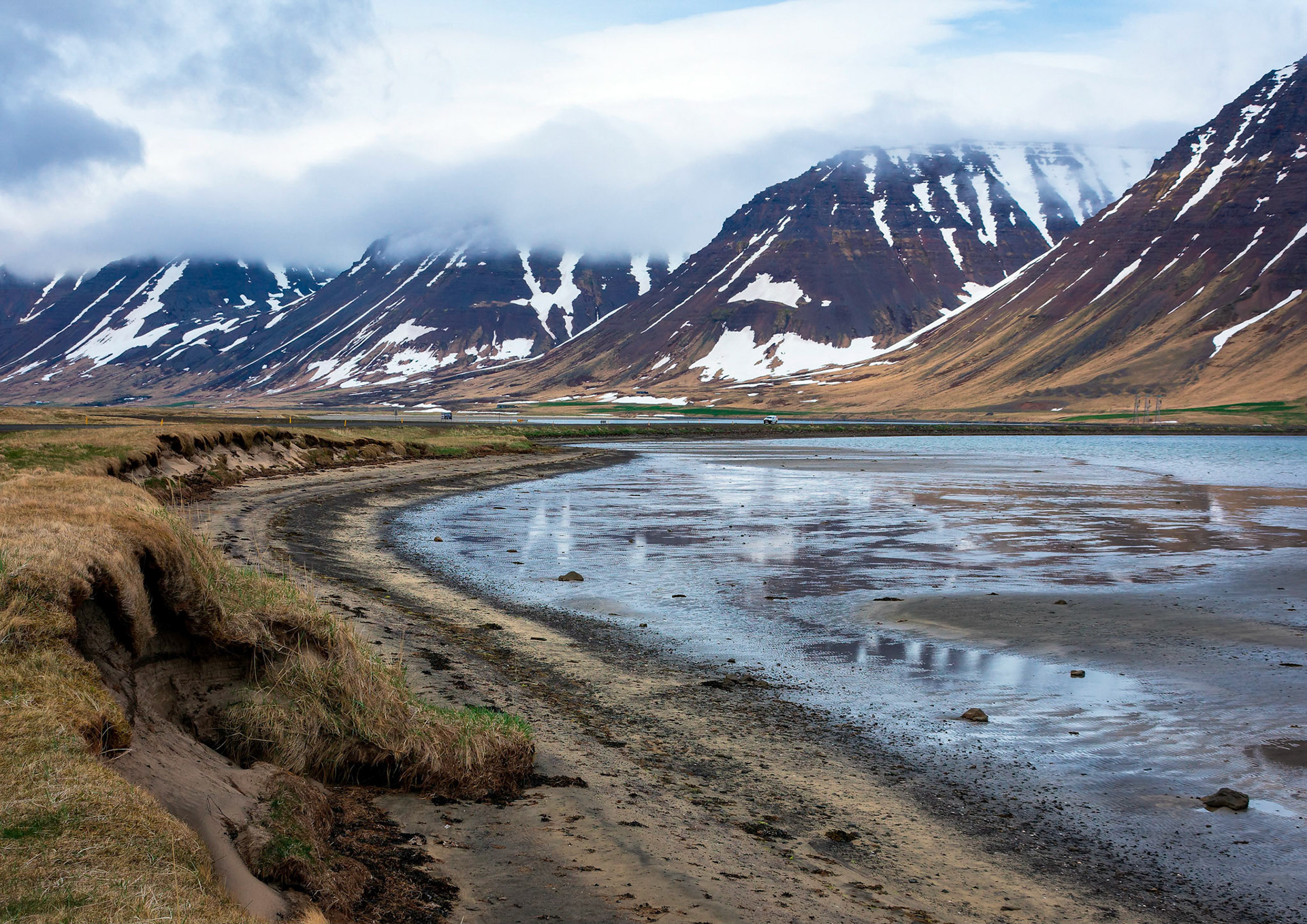 The beach near the settlement of Holt on Önundarfjörður, a fjord in the Icelandic region of Westfjords, sweeps out towards the ocean. The fjord is crossed by a causeway carrying the road to the town of Ísafjörður.