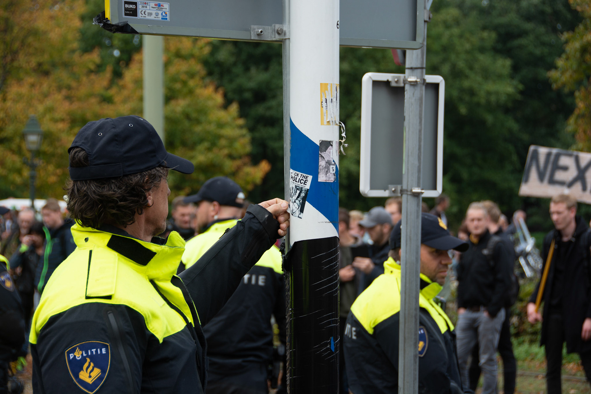Een politie agent probeert tijdens het boeren protest een sticker met "fuck the police"erop te verwijderen van een paal