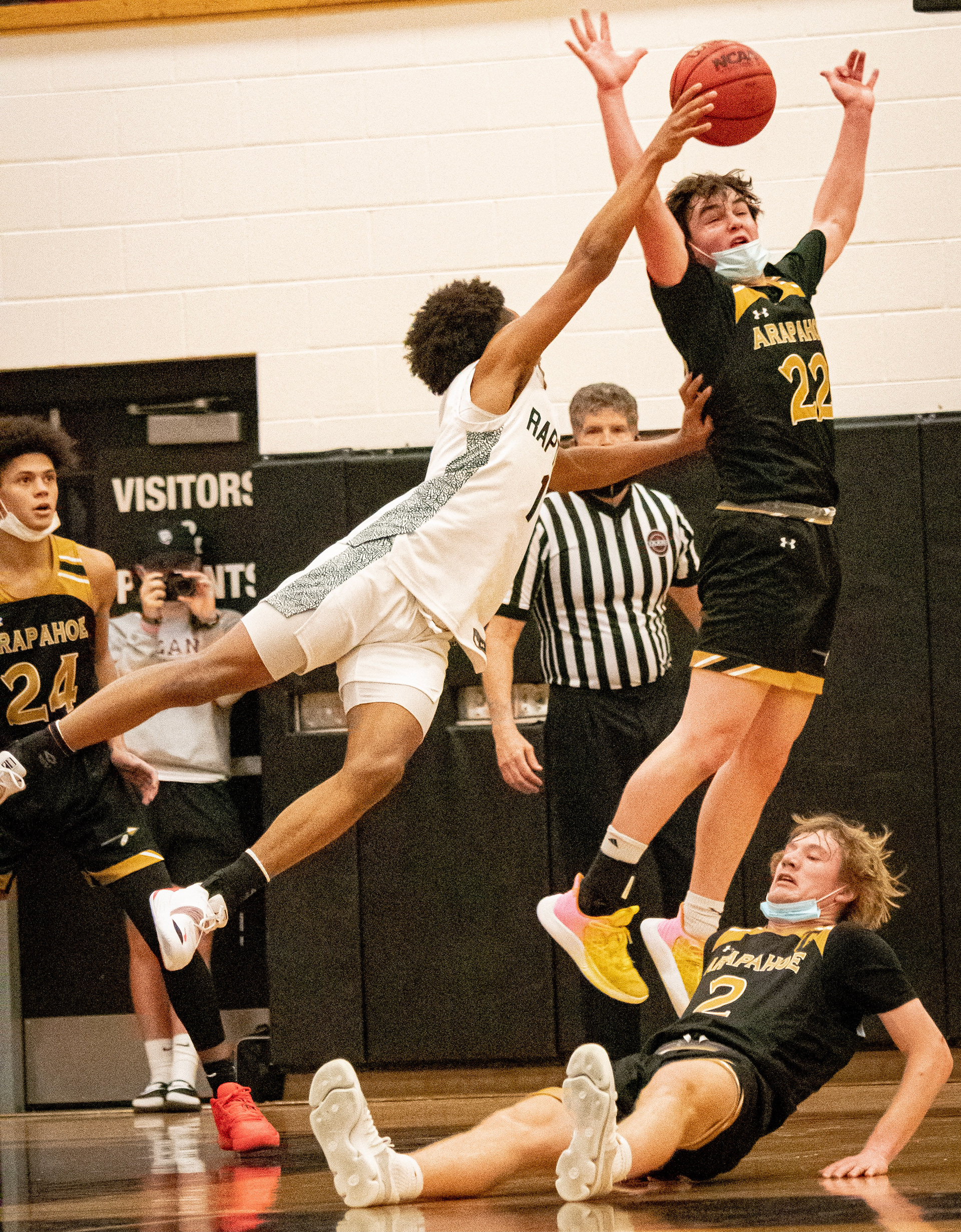 Arapahoe senior Kyle Sweeney (#22) blocks an attempted layup from the opposing team as Arapahoe senior Marshall Gueller (#2) is knocked to the court. Both seniors passionately contributed to many Arapahoe victories during the season while they mentored their younger teammates. 