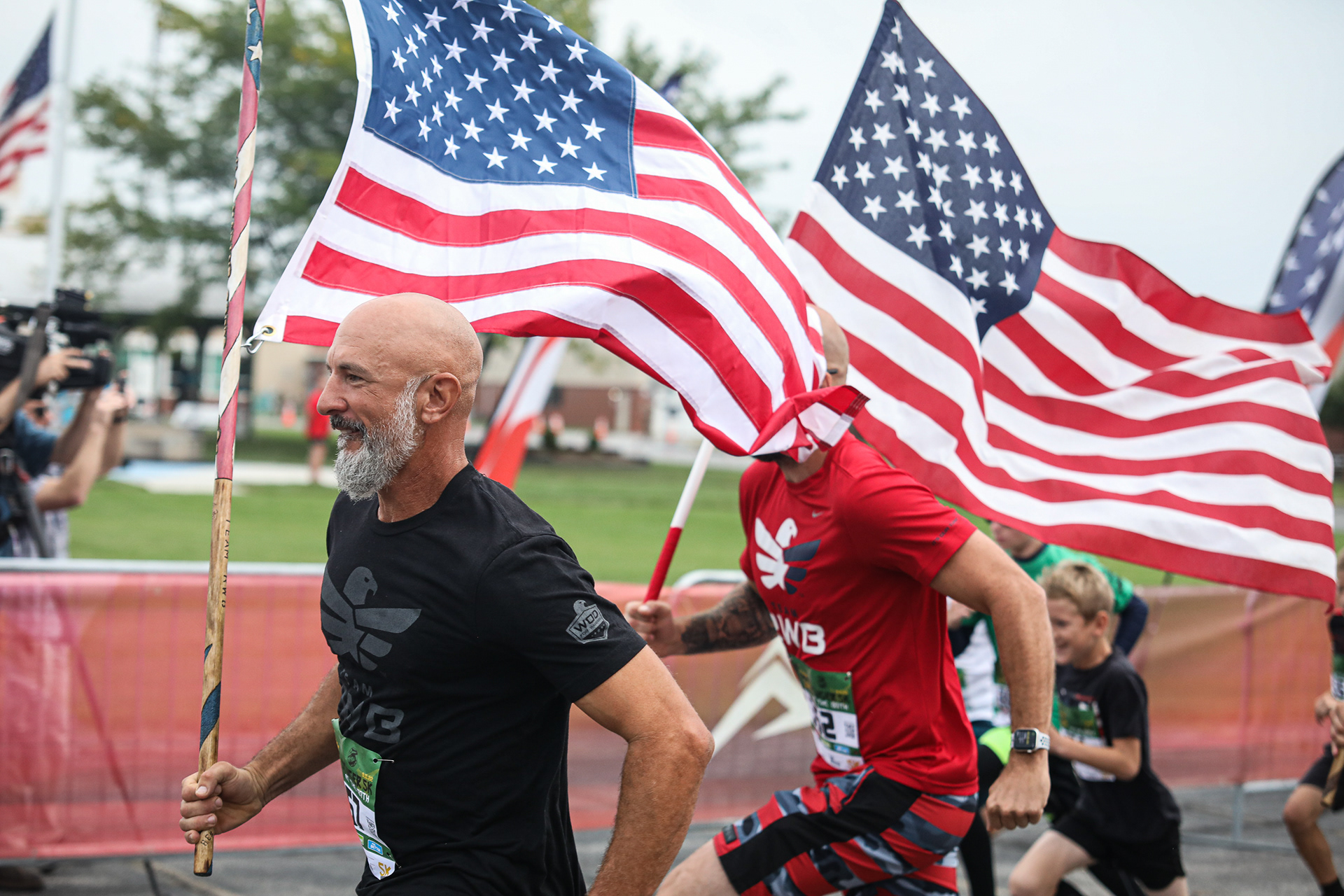 Jason Portala, left, smiles as he starts the race carrying an American flag at the Stinger 5k at 180th Fighter Wing, Ohio Air National Guard in Swanton, Ohio on Sunday, September 11, 2022. For Toledo Blade.