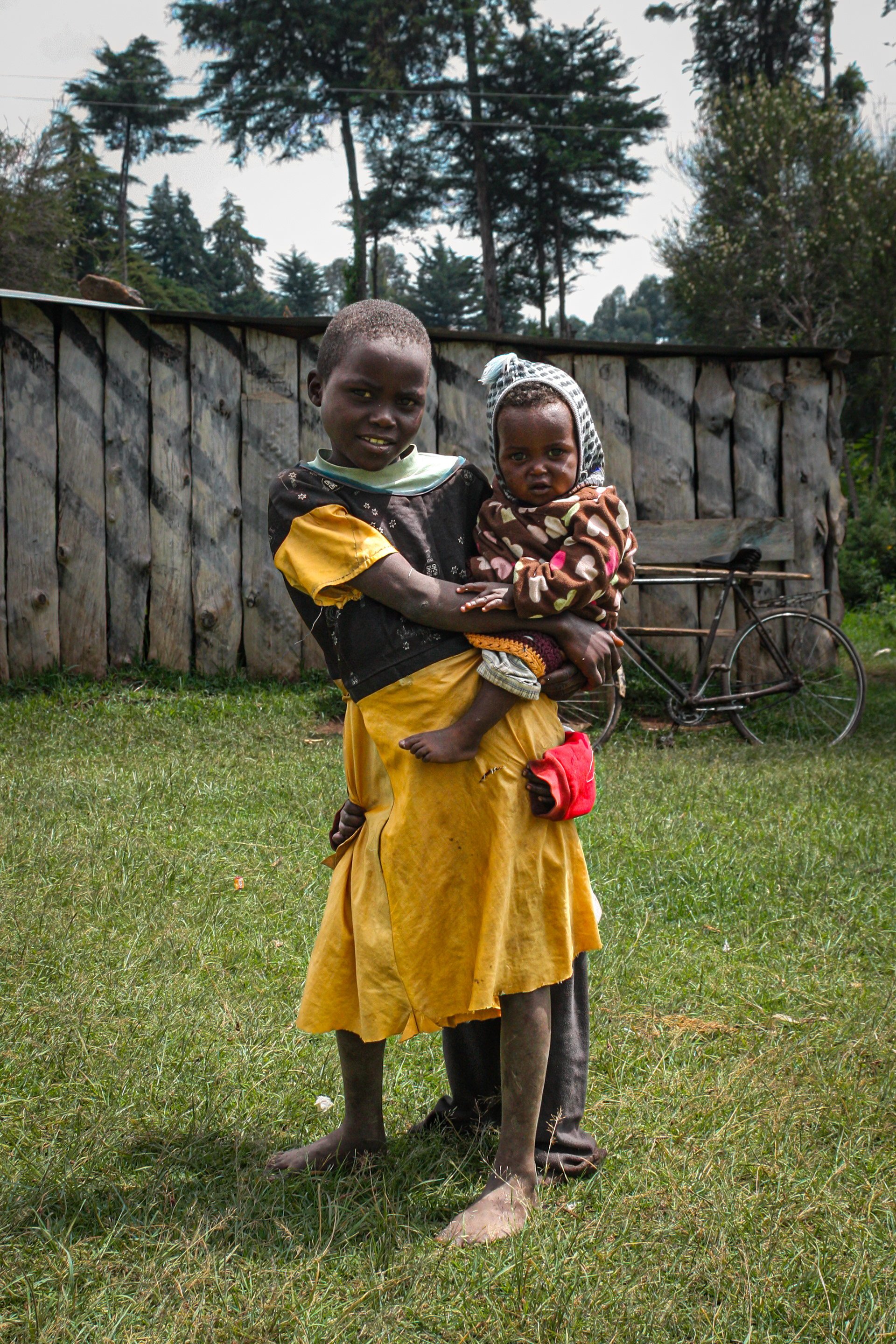 A young girl holds a small child while another hides behind her in Nakuru, Kenya in 2016.