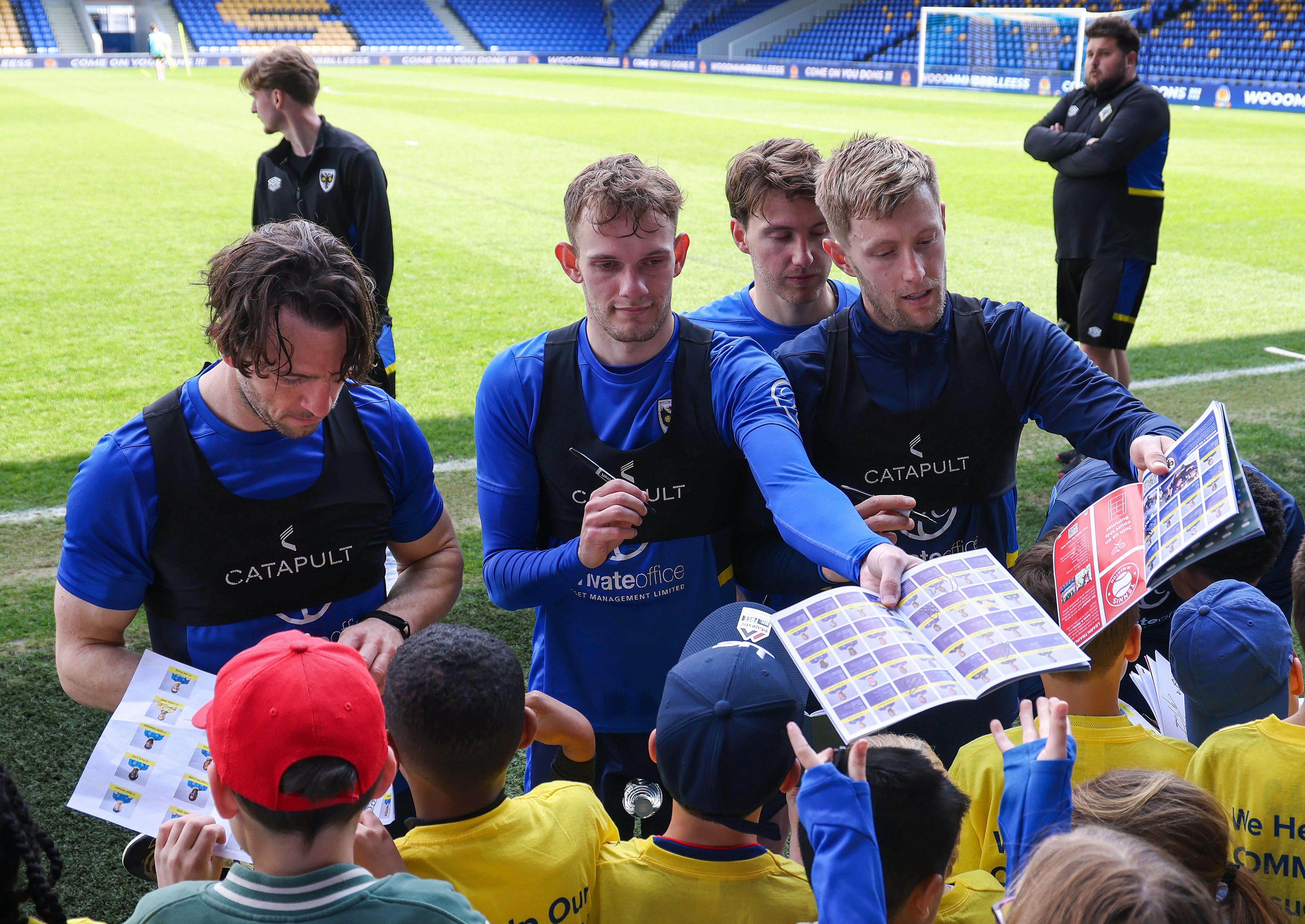 Players sign fans programmes following an AFC Wimbledon training session at The Cherry Red Records Stadium. Shot for Kontent Haus Agency