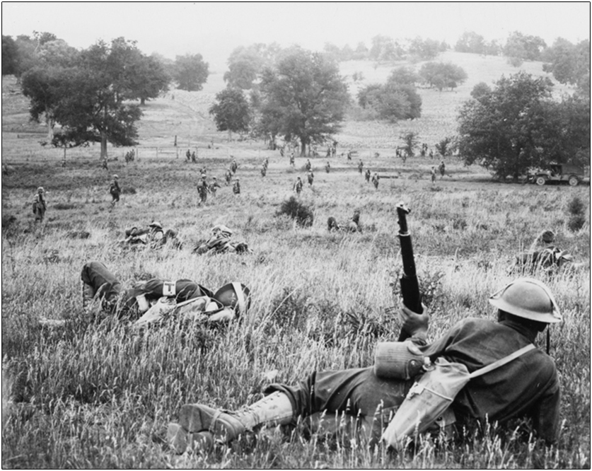 A grayscale photo of U.S. Army soldiers in a grassy landscape, with a view extending into the distance.