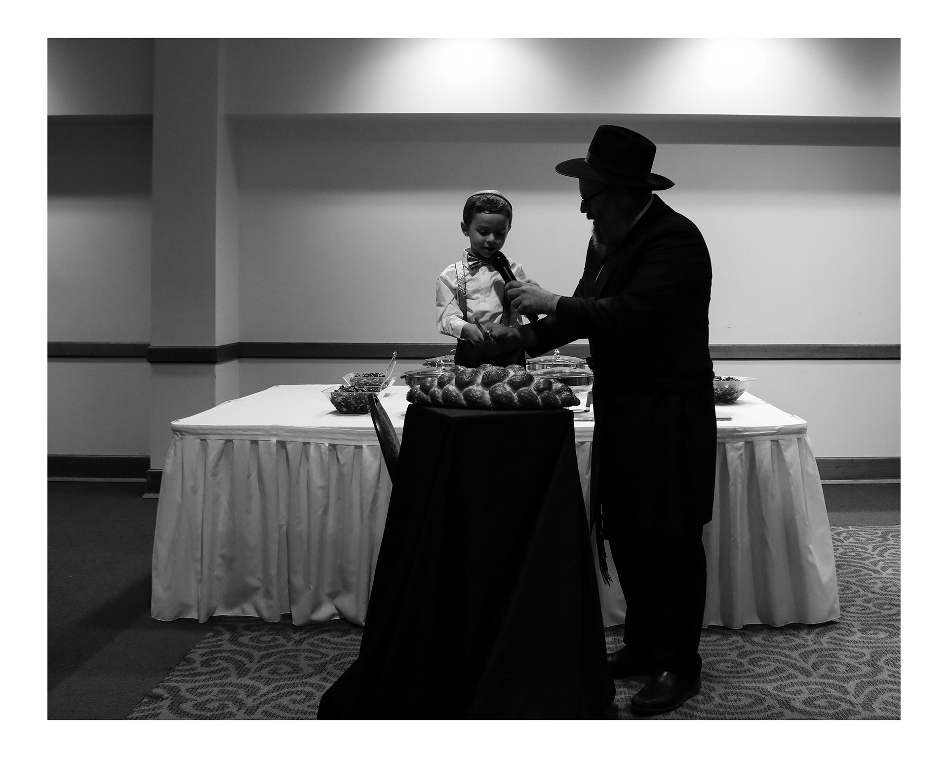 Rabbi Hendel Weingarten, right, holds the microphone for Levi to say a prayer before dinner at Chani's bat mitzvah.