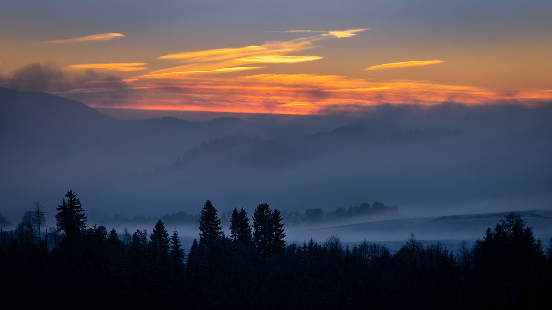 Sonnenuntergang bei aufziehendem Nebel in winterlicher Landschaft