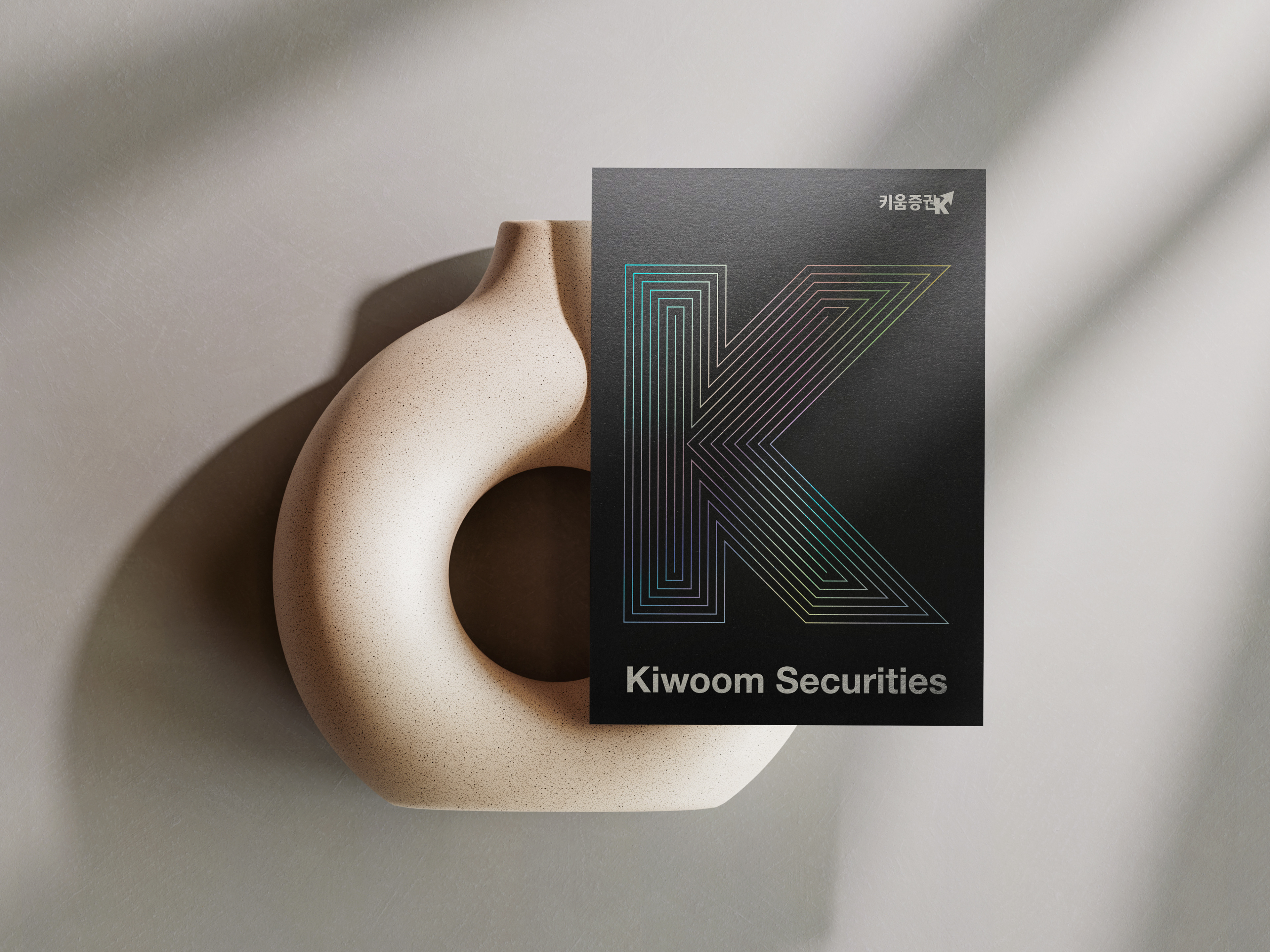 세라믹 오브제 위에 세운 키움증권 브로슈어—홀로그램 라인의 K 표지 Brochure mockup on ceramic object—Kiwoom cover featuring holographic line-art K