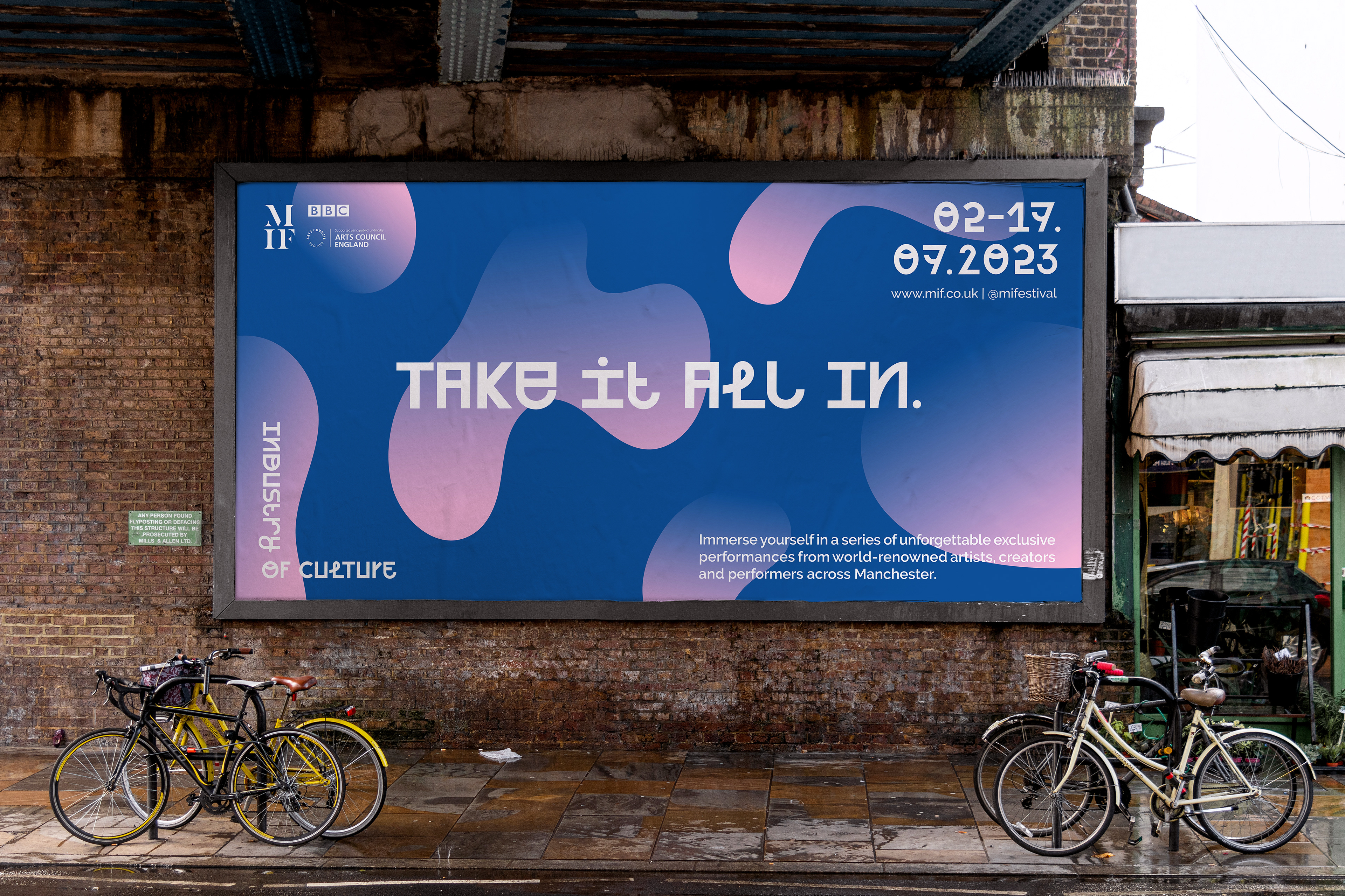 A billboard with the text take it all in which is under a bridge with some bikes in front