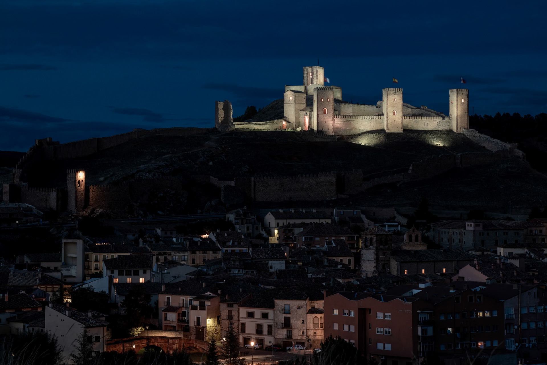 Illuminated medieval castle towering over a quiet village at night under a deep blue sky
