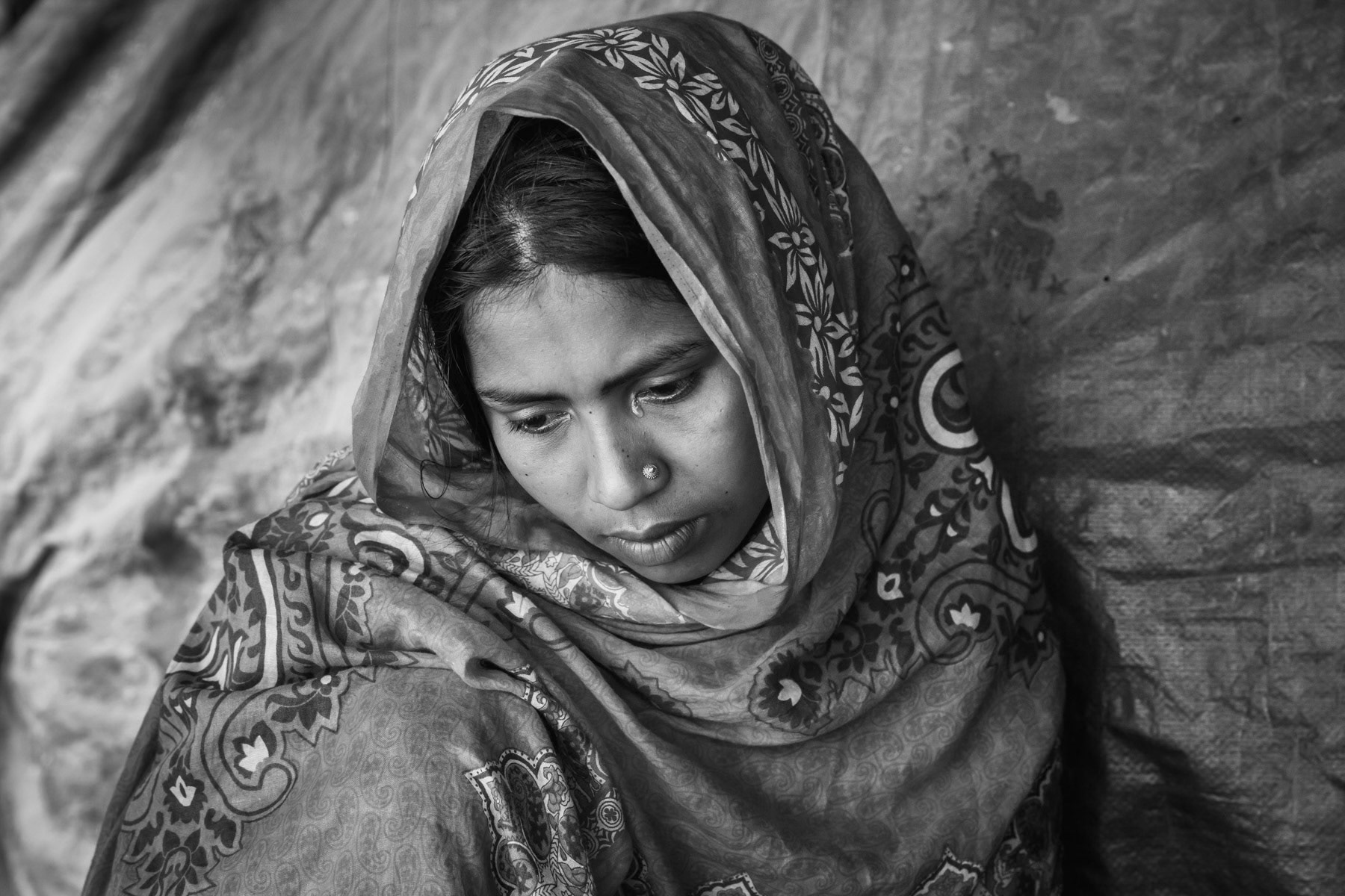 Hasina Begum, 20 years, from Chut Pyin, Rathedaung. Her husband was killed by Myanmar military during the attack on the village. She has one son and one daughter and fled with them and her parents to Bangladesh. Days before the attack they were forbidden to leave to buy food in the market and were basically under a 24 hours curfew within the village. The curfew was implemented by local Rakhine mobs, they didnt expect though what would follow. During the attack on the village about 120 villagers were collected and men and women were separated in the fields. More than 100 military were present. About 50 women were abducted and taken away to be raped. Their husbands were executed on the spot. Her baby who was with her, was taken away and given to her mother. All women (about 50) were taken to the local school building. Before being raped they were stripped searched for money and gold. While being raped they were putting heavy logs on their bodies so they wouldnt move. They were gang raped for 2 days. More than 100 military and locals were present in the school, maybe more groups passed during the 2 days. most of the time the women would be semi consicious. During the second night around 2AM, 5 of them including Hasina decided to try escaping through a back door. They were barely dressed and disorientated. Eventually they found their surviving families hiding in the jungle surrounding their village. The next early morning they all fled to Bangladesh where she now lives with her parents, one brother and 2 children. Chut Pyin village is one of the numerous Rohingya villages that have been totally wiped out and where severe acts of ethnic cleansing with genocidal intend have been committed by the military and local mobs. Hundreds of Rohingya have been massacred in this village alone. Tangkhali camp, Bangladesh, March 2018