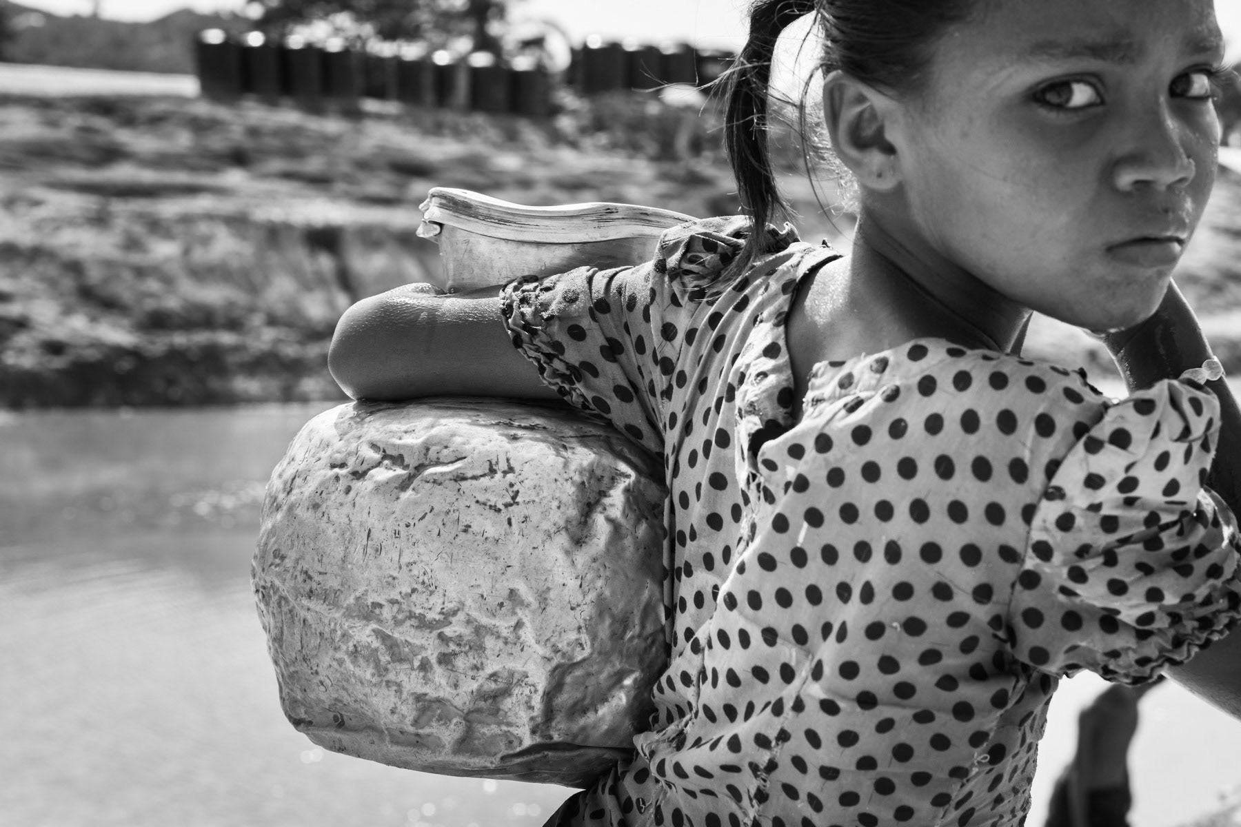 A Rohingya girl carrying the little water remaining in the ponds at the end of the dry season. The lack of rain water makes people pump water from the river which is consumed untreated, causing high levels of diarrhea among the camp population. Kyin Ni Pyin IDP Camp, Rakhine, Myanmar, May 2017
