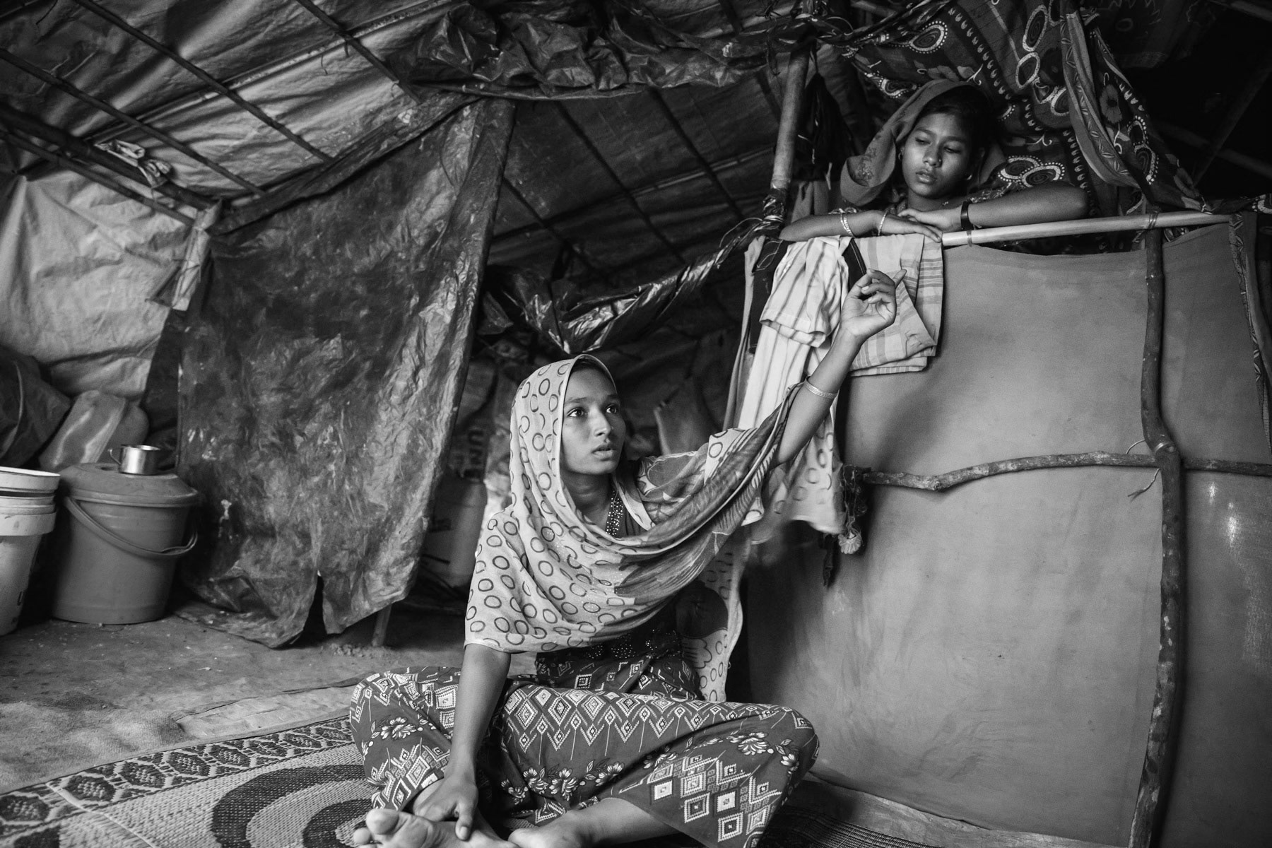 Fatima Khatun, 20 years old and her sister from Shilhadi in Rathedaung township. She has one daughter and one son, her husband was arrested by the military and jailed 8 months ago. Their village was attacked begining September 2017 by military forces. During the attack her sister in law and her two children were executed and decapitated in front of her. She managed to escape but was shot in the leg. Her mother had left the village before the attack with her 2 children. The village was attacked by at least 100 military forces aided by local Rakhine extremists. The extremists were decapitating people. Eight hundred Rohingya were living in her village, all fled or were killed and the village was burnt down. It took her 18 days to reach Bangladesh helped by her sister and her brother in law. She got the first medical care after having reached Bangladesh and still faces difficulties to walk. She has been without news from her husband for the past 6 months. Kutupalong camp, Cox's Bazar, Bangladesh, November 2017