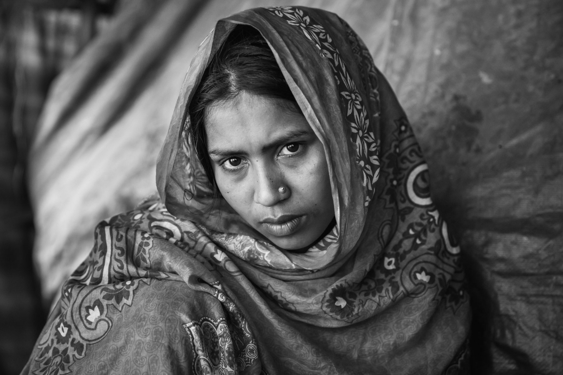 Hasina Begum, 20 years, from Chut Pyin, Rathedaung. Her husband was killed by Myanmar military during the attack on the village. She has one son and one daughter and fled with them and her parents to Bangladesh. Days before the attack they were forbidden to leave to buy food in the market and were basically under a 24 hours curfew within the village. The curfew was implemented by local Rakhine mobs, they didnt expect though what would follow. During the attack on the village about 120 villagers were collected and men and women were separated in the fields. More than 100 military were present. About 50 women were abducted and taken away to be raped. Their husbands were executed on the spot. Her baby who was with her, was taken away and given to her mother. All women (about 50) were taken to the local school building. Before being raped they were stripped searched for money and gold. While being raped they were putting heavy logs on their bodies so they wouldnt move. They were gang raped for 2 days. More than 100 military and locals were present in the school, maybe more groups passed during the 2 days. most of the time the women would be semi consicious. During the second night around 2AM, 5 of them including Hasina decided to try escaping through a back door. They were barely dressed and disorientated. Eventually they found their surviving families hiding in the jungle surrounding their village. The next early morning they all fled to Bangladesh where she now lives with her parents, one brother and 2 children. Chut Pyin village is one of the numerous Rohingya villages that have been totally wiped out and where severe acts of ethnic cleansing with genocidal intend have been committed by the military and local mobs. Hundreds of Rohingya have been massacred in this village alone. Tangkhali camp, Bangladesh, March 2018