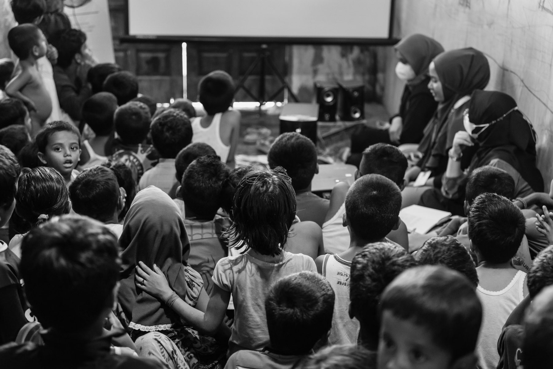 Rohingya refugees watching a movie in a refugee center. They have recently arrived by boat from Bangladesh, a journey that takes several weeks in overcrowded wooden boats. The Rohingya flee persecution and conflict in Myanmar. The Aceh region on the island of Sumatra in Indonesia is seen by many as a safe place from where they may have better opportunities and safety than in the refugee camps in Bangladesh. Lhokseumawe refugee center, Aceh, Indonesia, February 2024 than in the refugee camps in Bangladesh. Lhokseumawe refugee center, Aceh, Indonesia, February 2024