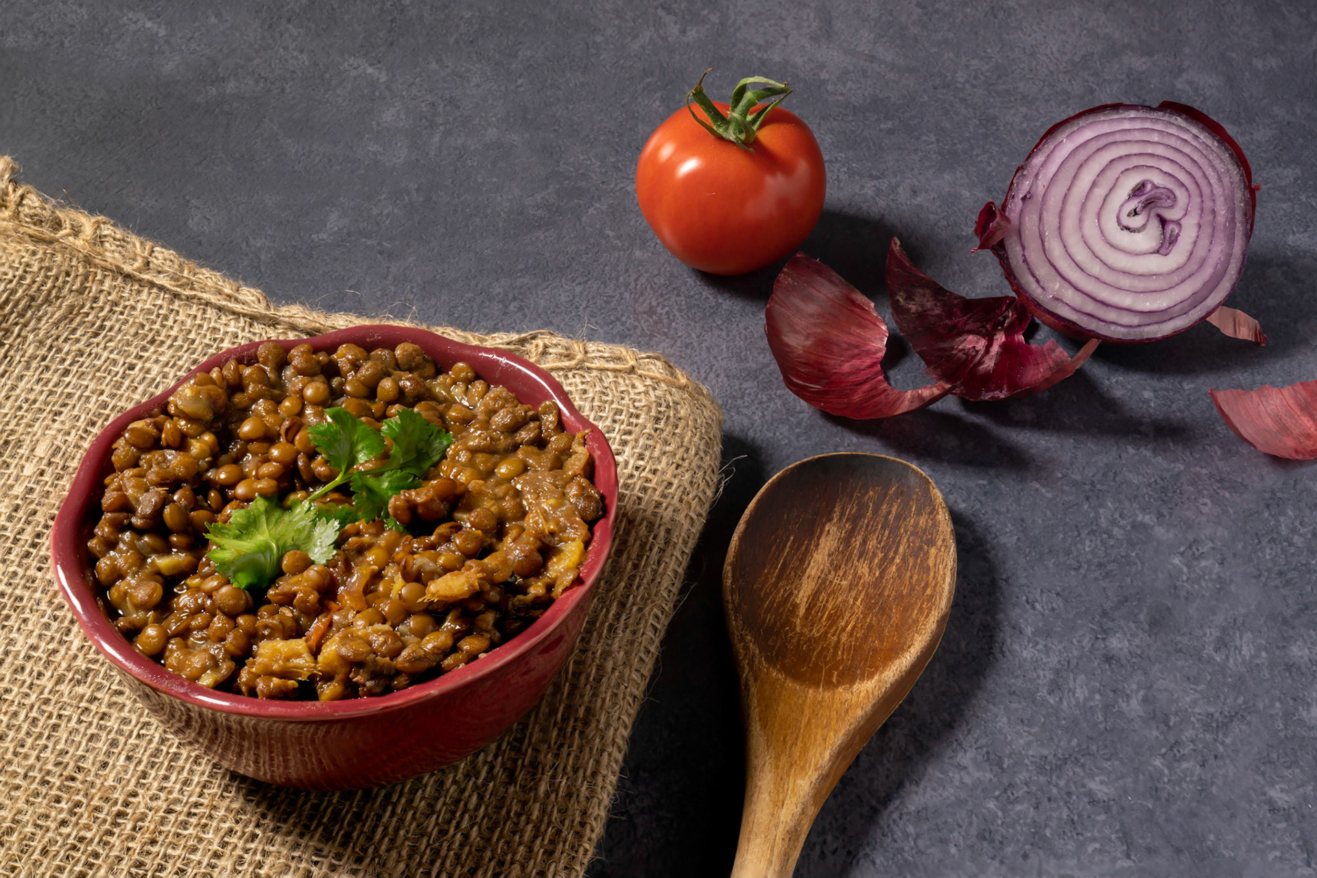 Homemade spicy brown lentil or masoor dal soup with coriander, red onion and tomato in a bowl. Indian brown lentil curry.
